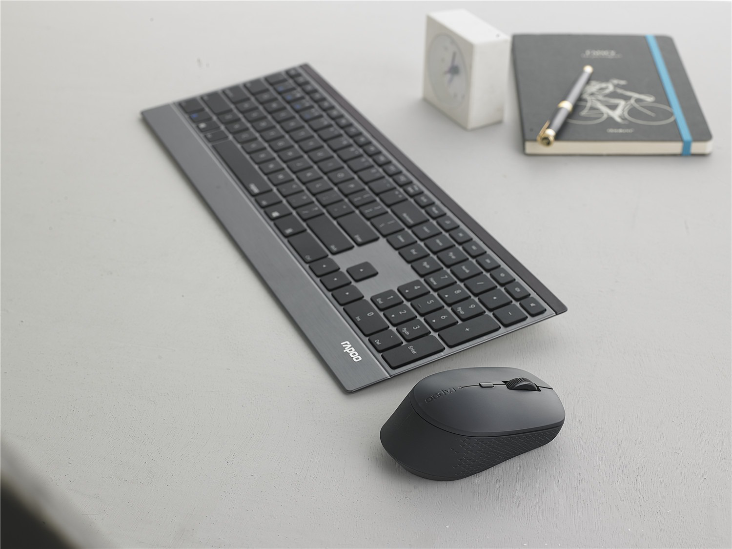 Clavier et souris sur une surface grise avec un cahier et un stylo.