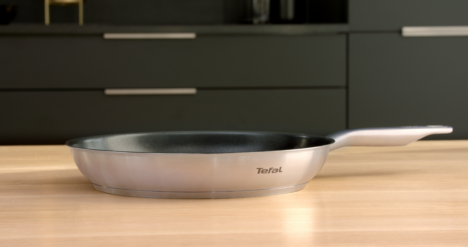 Zilveren koekenpan met een zwart interieur, op een houten oppervlak.