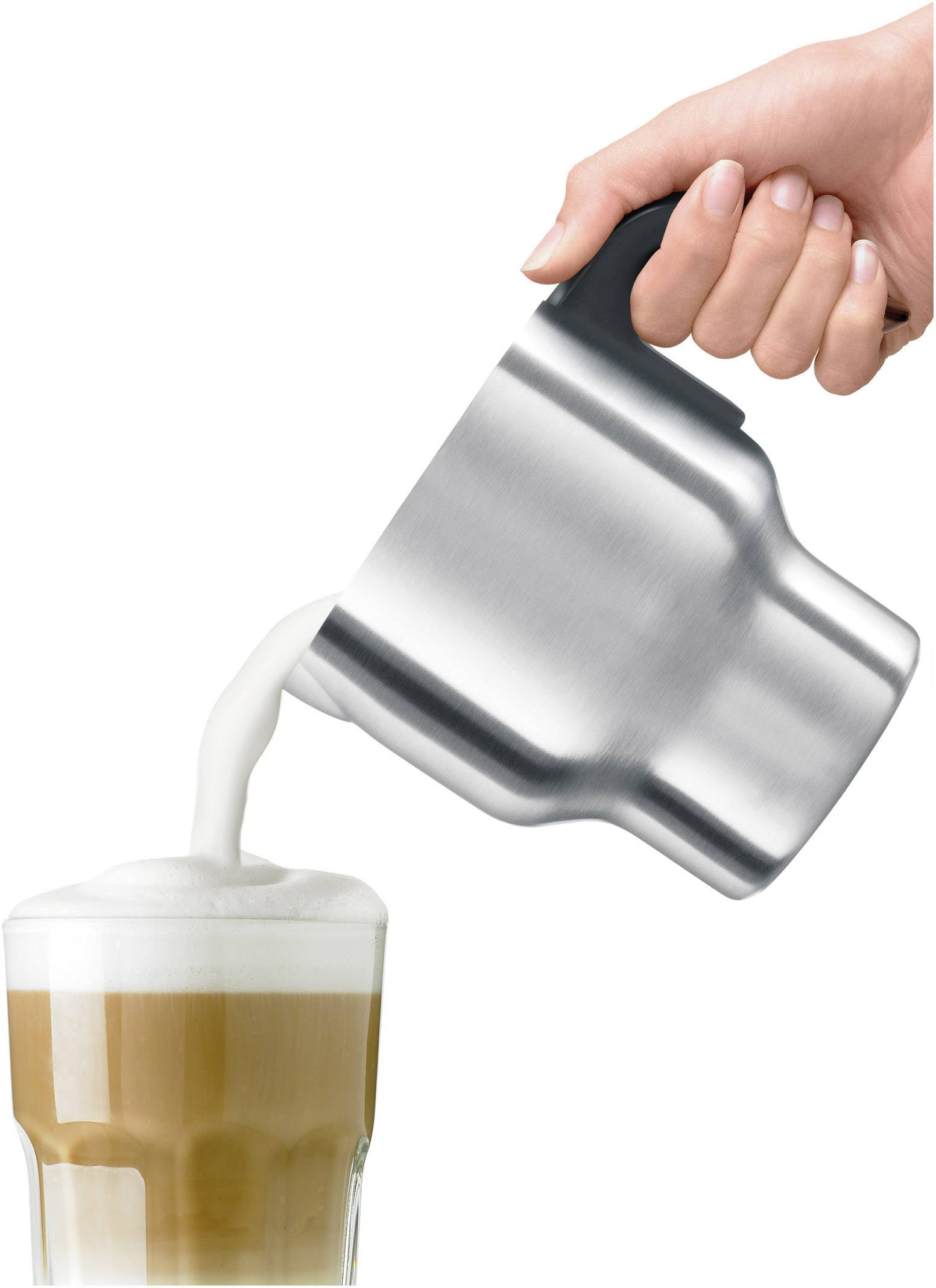 A person pouring frothed milk from a stainless steel pitcher into a glass of latte.