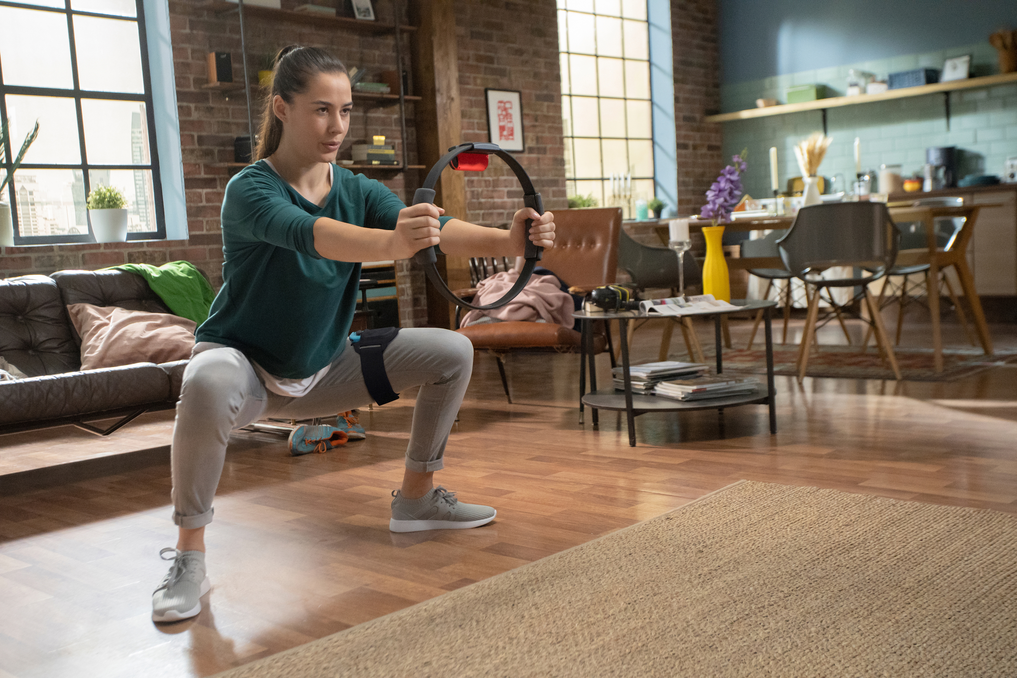 Frau in einem Wohnzimmer, die mit einem ringförmigen Fitnessgerät trainiert.