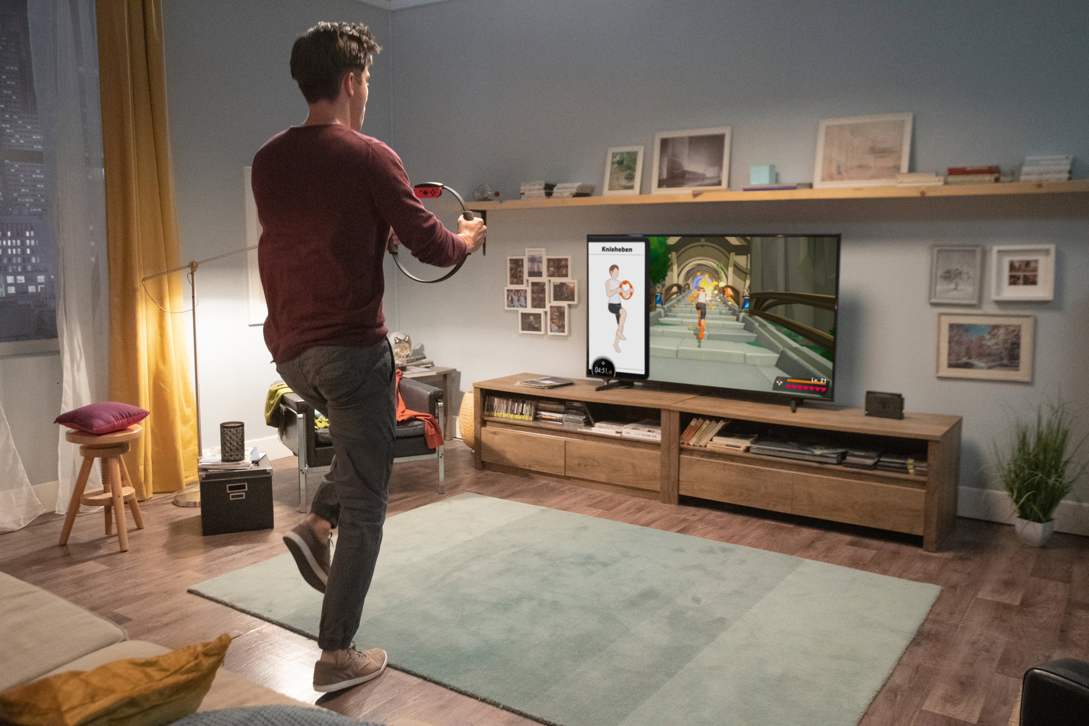 Mann, der mit einem ringförmigen Controller in einem Wohnzimmer trainiert. TV zeigt ein Fitnessspiel.