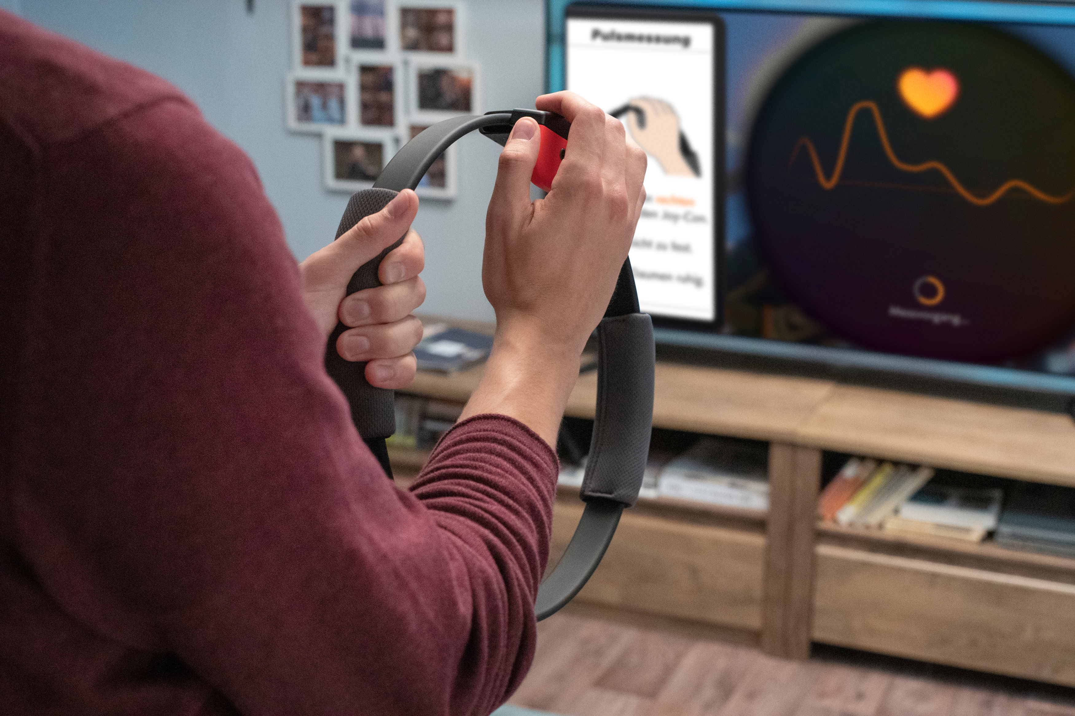 Person hält ringförmiges Trainingsgerät, schaut auf Fernsehbildschirm mit Trainings-Oberfläche.