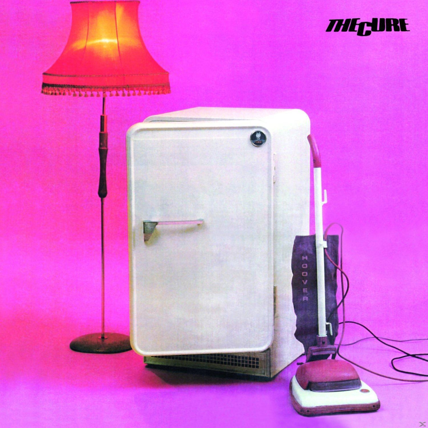 Pochette d'album : album de The Cure, réfrigérateur blanc, lampe, aspirateur, fond rose.