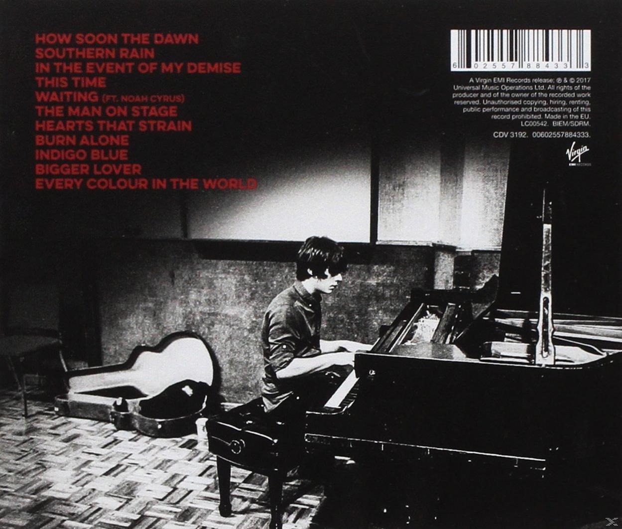 Monochroom beeld van een man die piano speelt, met een gitaar en bladmuziek aan de zijkant.