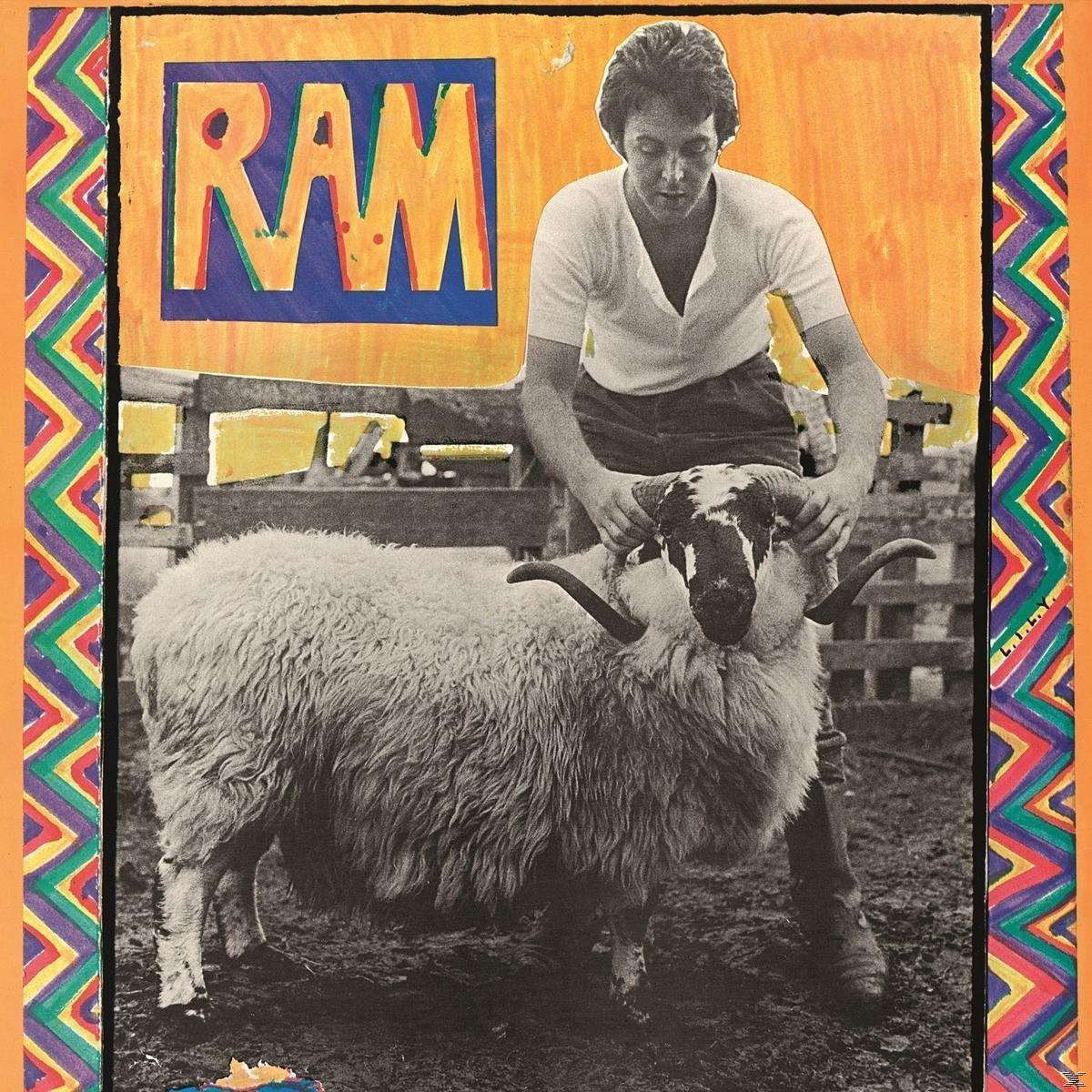 Mann hält ein Schaf an den Hörnern, oben steht das Wort 'RAM', in einem bunten Rahmen.