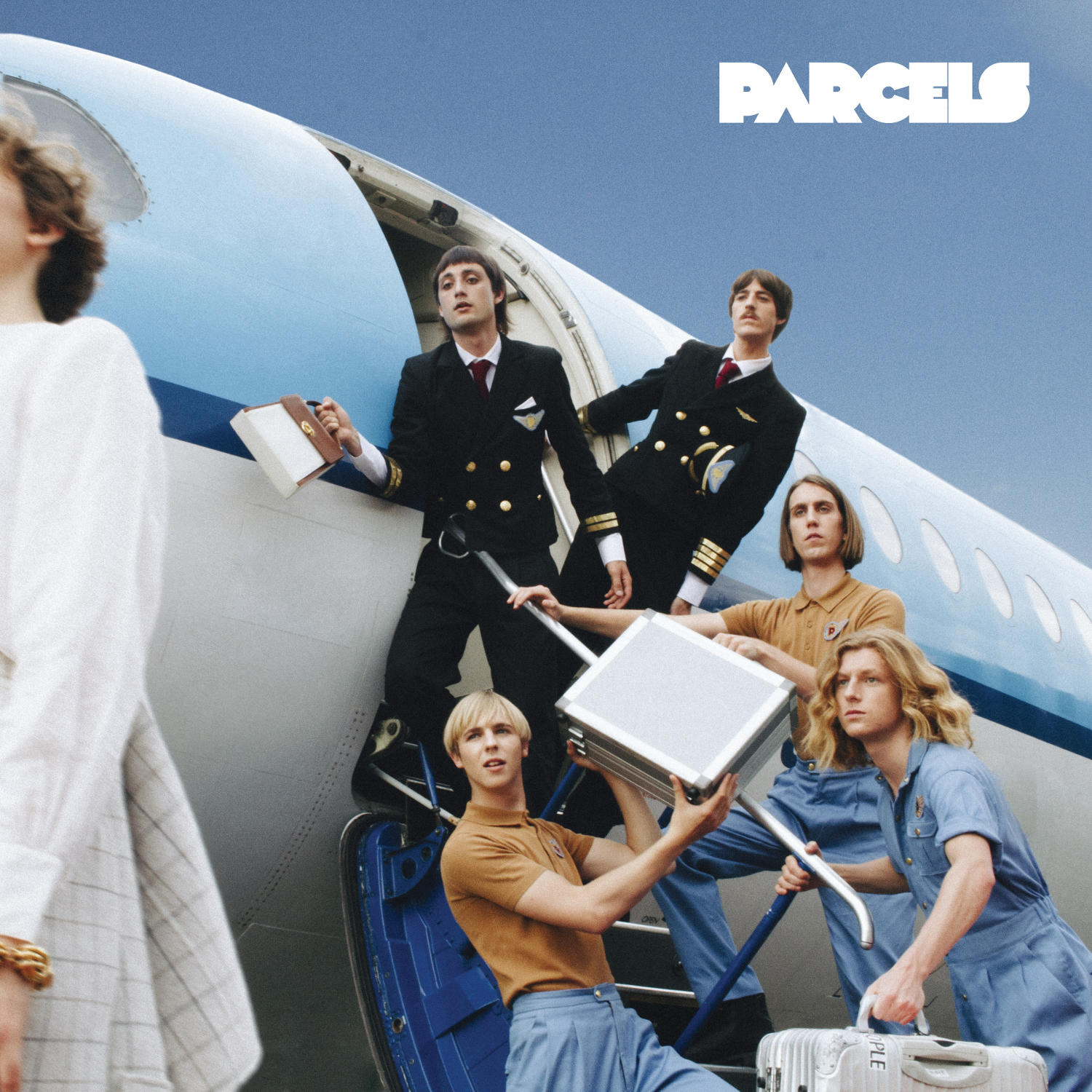 Albumcover zeigt eine Band, die ein Flugzeug verlässt. Der Titel "PARCELS" ist sichtbar.