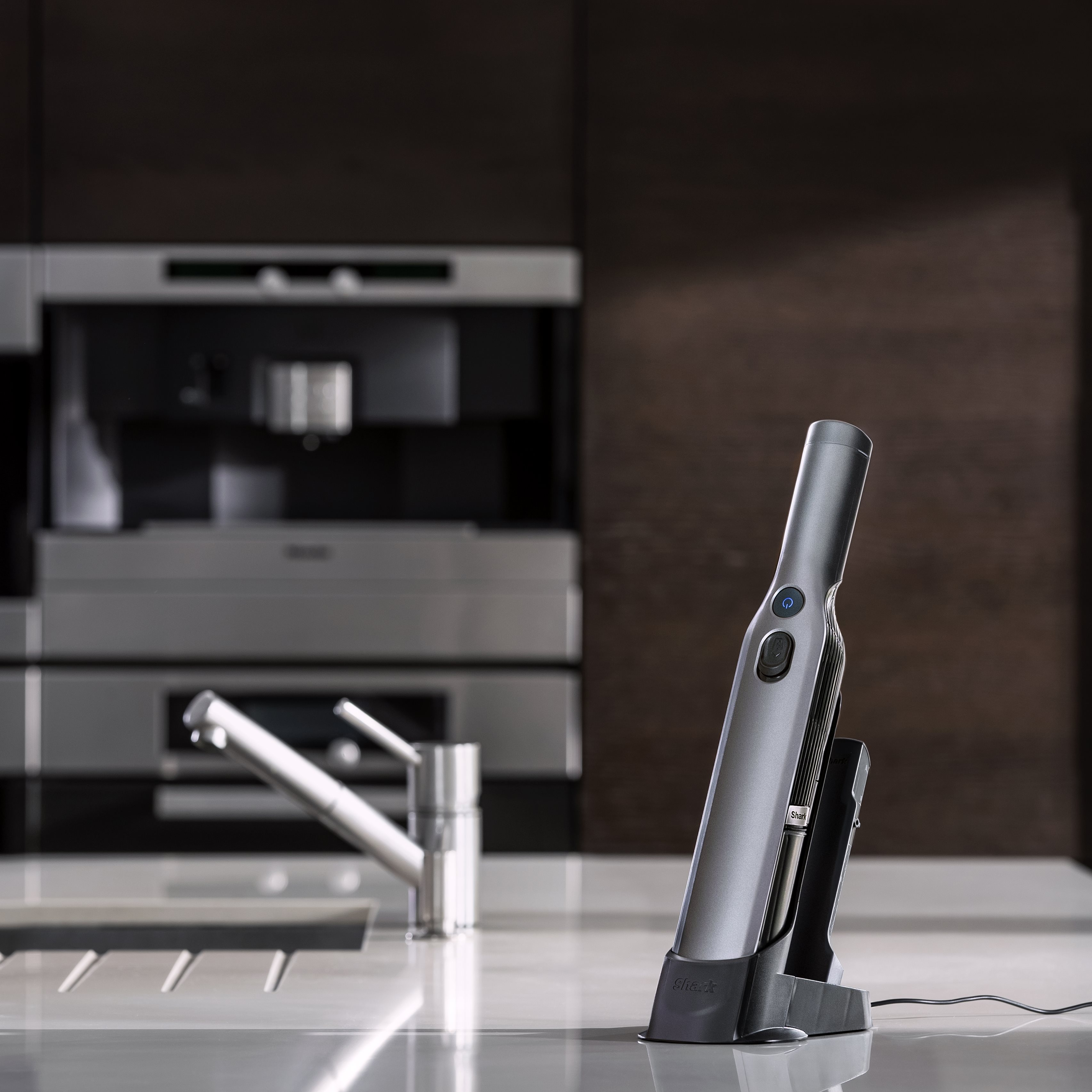 Un aspirateur à main Shark argent et gris sur un comptoir blanc dans un cadre de cuisine.