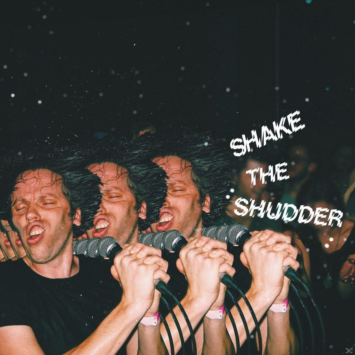 Quatre hommes chantant dans des micros sur scène, avec les mots SHAKE THE SHUDDER écrits à droite.