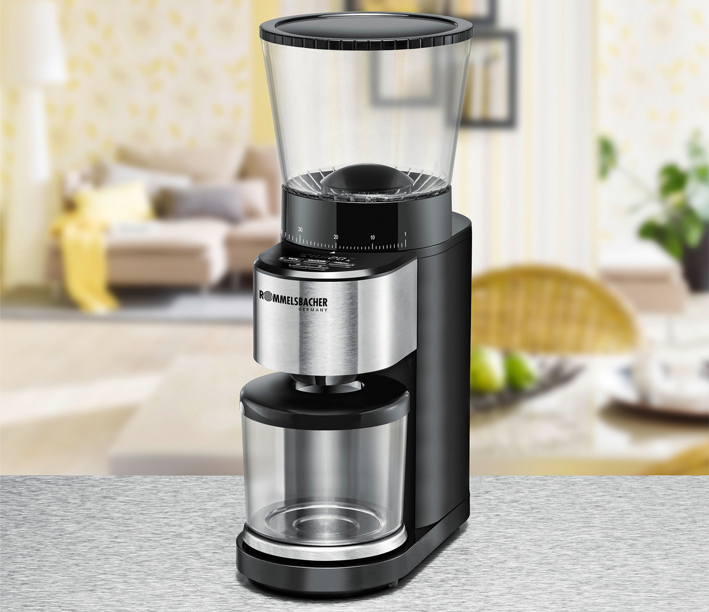Kaffeemühle auf einem Tisch, vor einer verschwommenen Wohnzimmerszene. Schwarz- und Silberfarben.