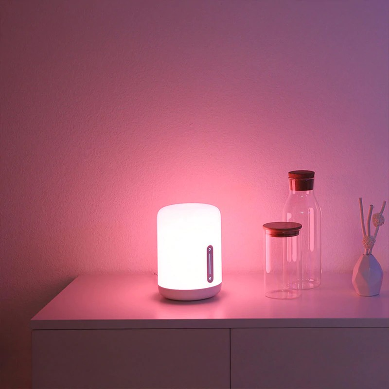 Lámpara blanca con brillo rosa en una mesa blanca con botellas.