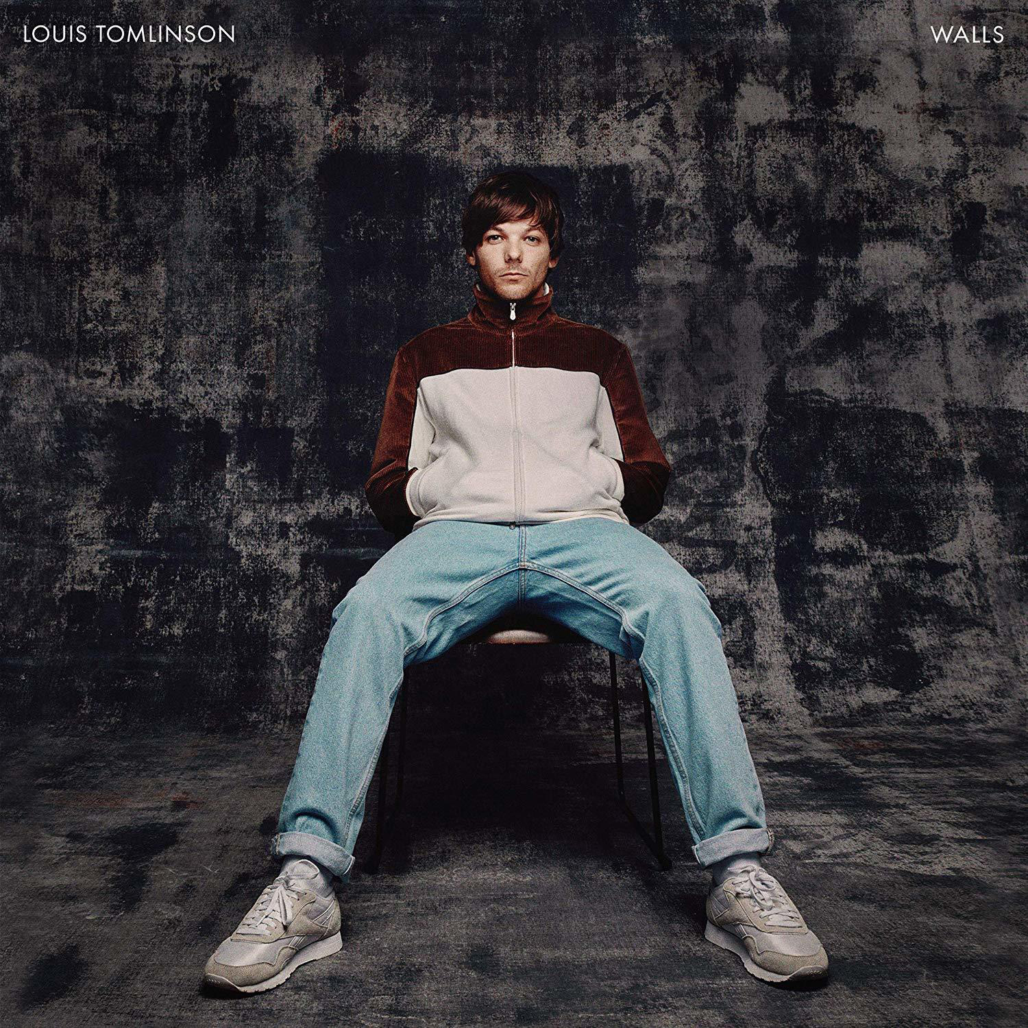 Louis Tomlinson Albumcover. Er sitzt in einer Jacke und Jeans auf einem Stuhl vor einer dunklen, strukturierten Wand.