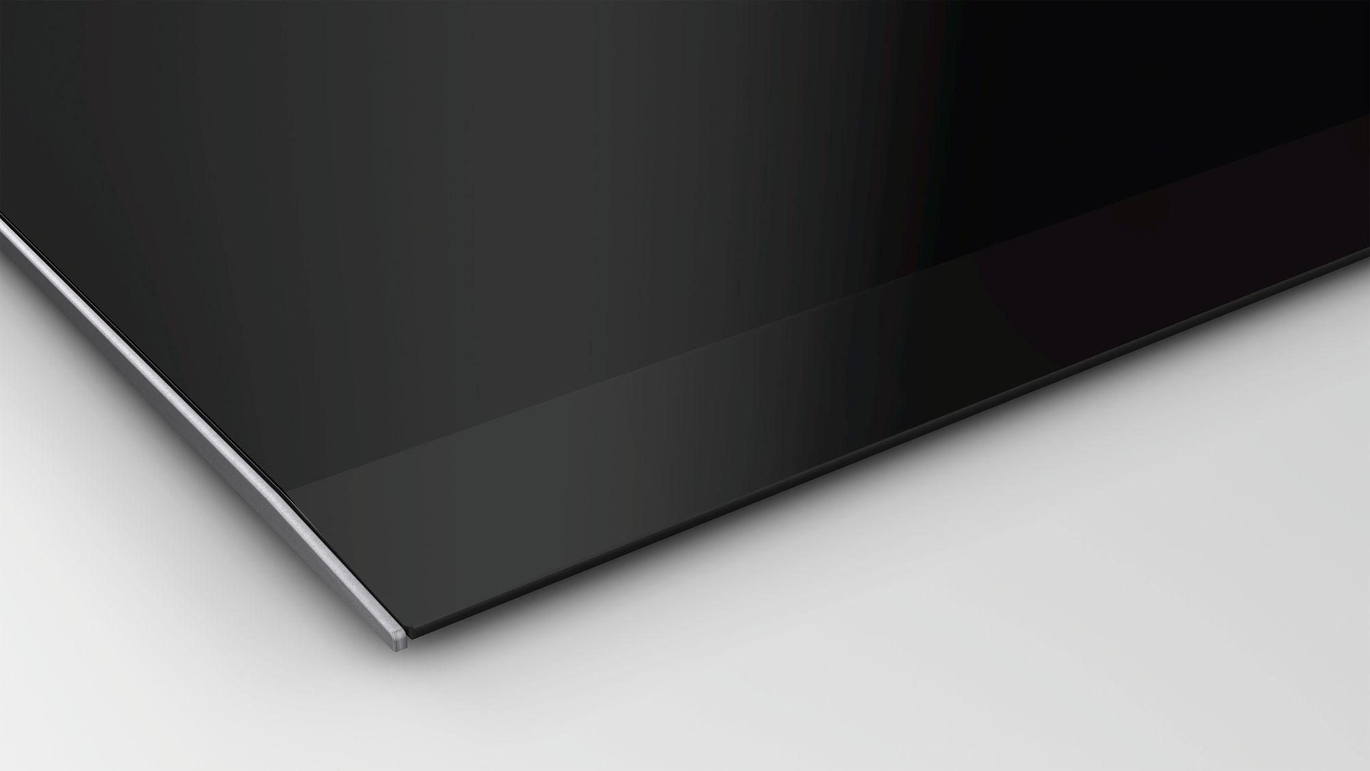 Gros plan d'une plaque de cuisson en verre noir avec un bord métallique, sur une surface blanche.