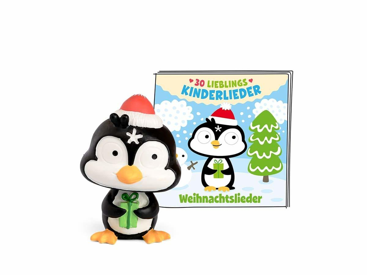 Ein Pinguinspielzeug mit roter Mütze und Geschenk steht neben einem Buch mit Pinguin, Weihnachtsbaum und Text.