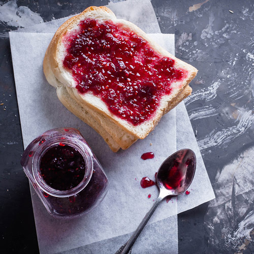 Toast mit Marmelade und ein Marmeladenglas. Löffel mit Marmelade auf dunkler, strukturierter Oberfläche.