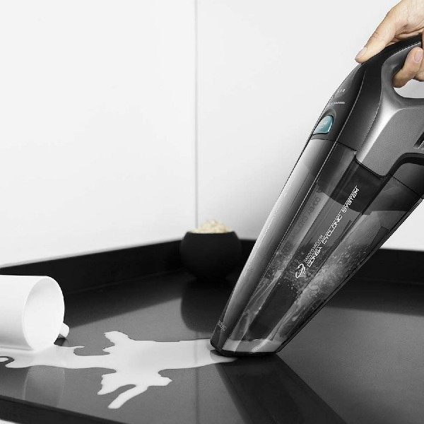 Una mano aspirando una superficie negra donde se derramó agua, con una taza blanca cerca.