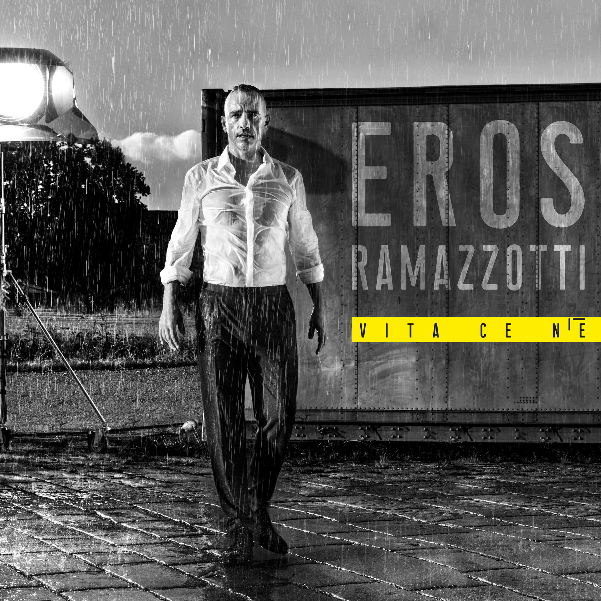 Eros Ramazzotti esőben, egy konténer előtt áll, album borító.