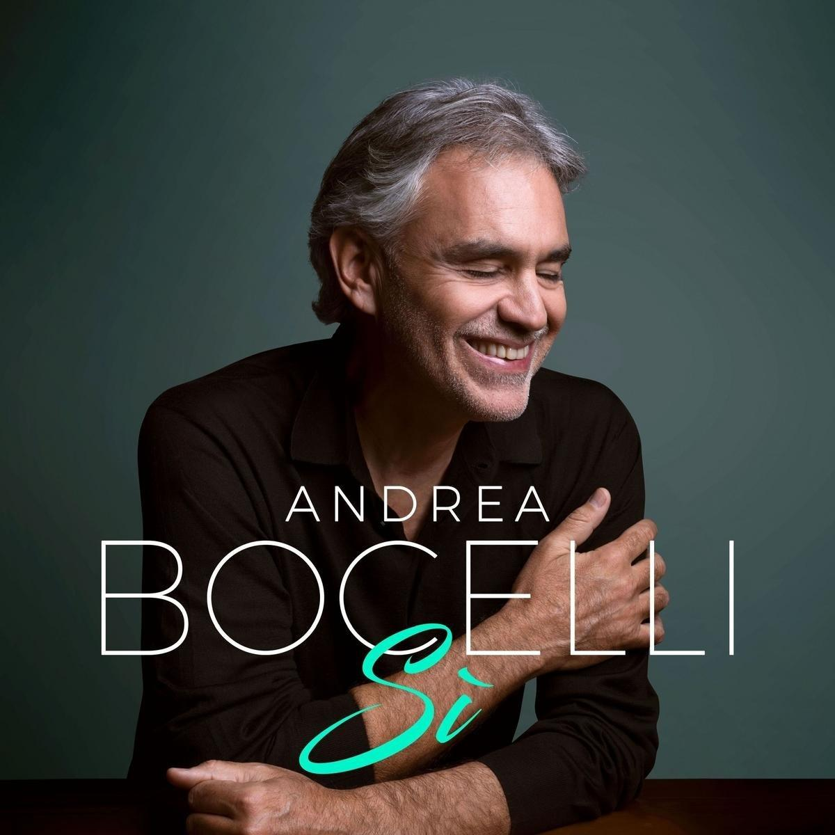 Andrea Bocelli glimlacht met gekruiste armen. De tekst is Andrea Bocelli Si.