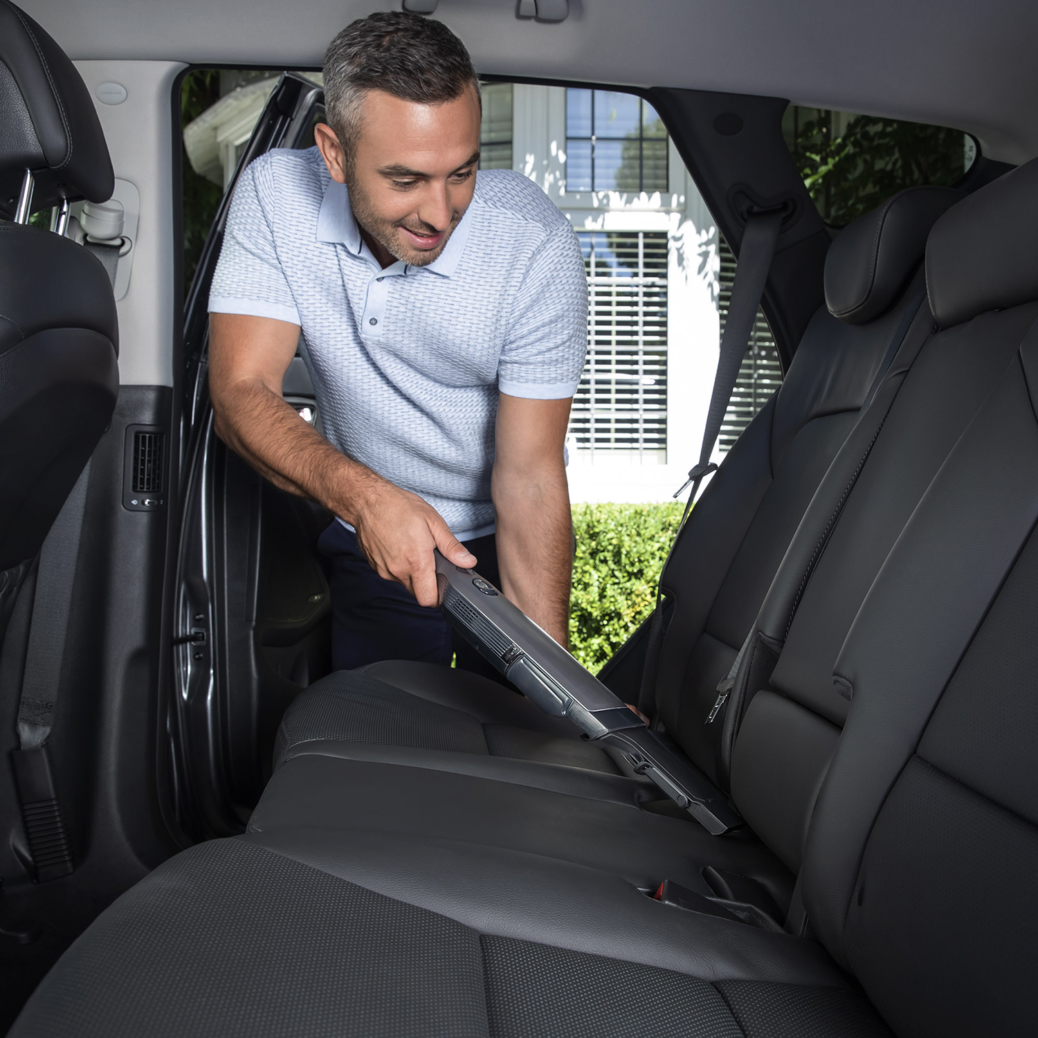 A man vacuuming a car seat. The car interior is visible and well-lit.