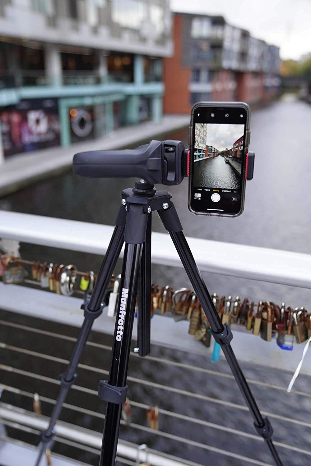 Ein Telefon auf einem Stativ, das einen Kanal filmt. Der Hintergrund zeigt Gebäude und eine Brücke mit Schlössern.