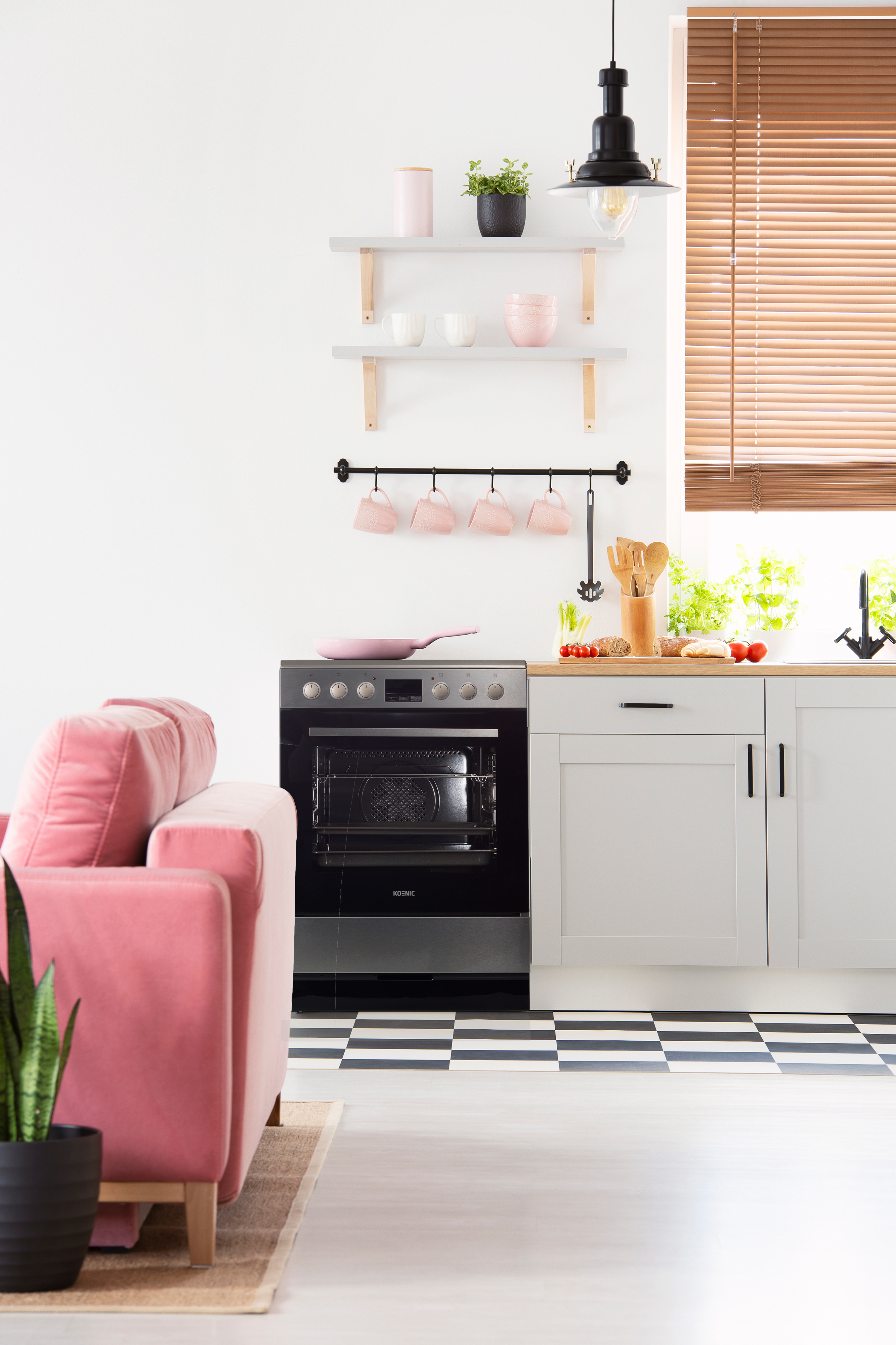 Eine Küchenszene mit einem pinkfarbenen Sofa, Ofen, Regalen und einem karierten Boden.