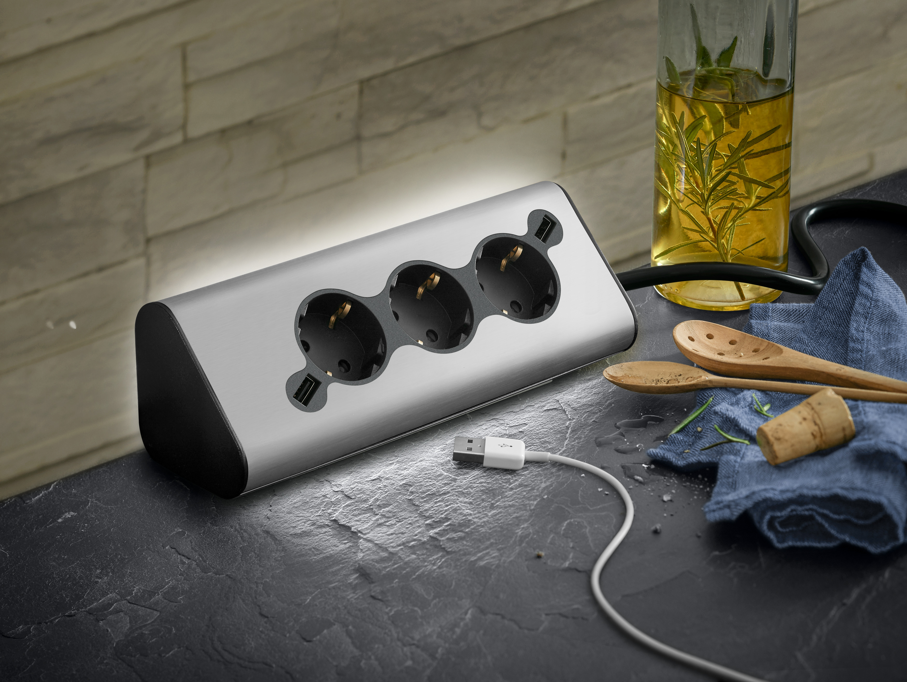 Silberne Steckdosenleiste mit drei Steckdosen und zwei USB-Anschlüssen, mit Kabel und Flasche.