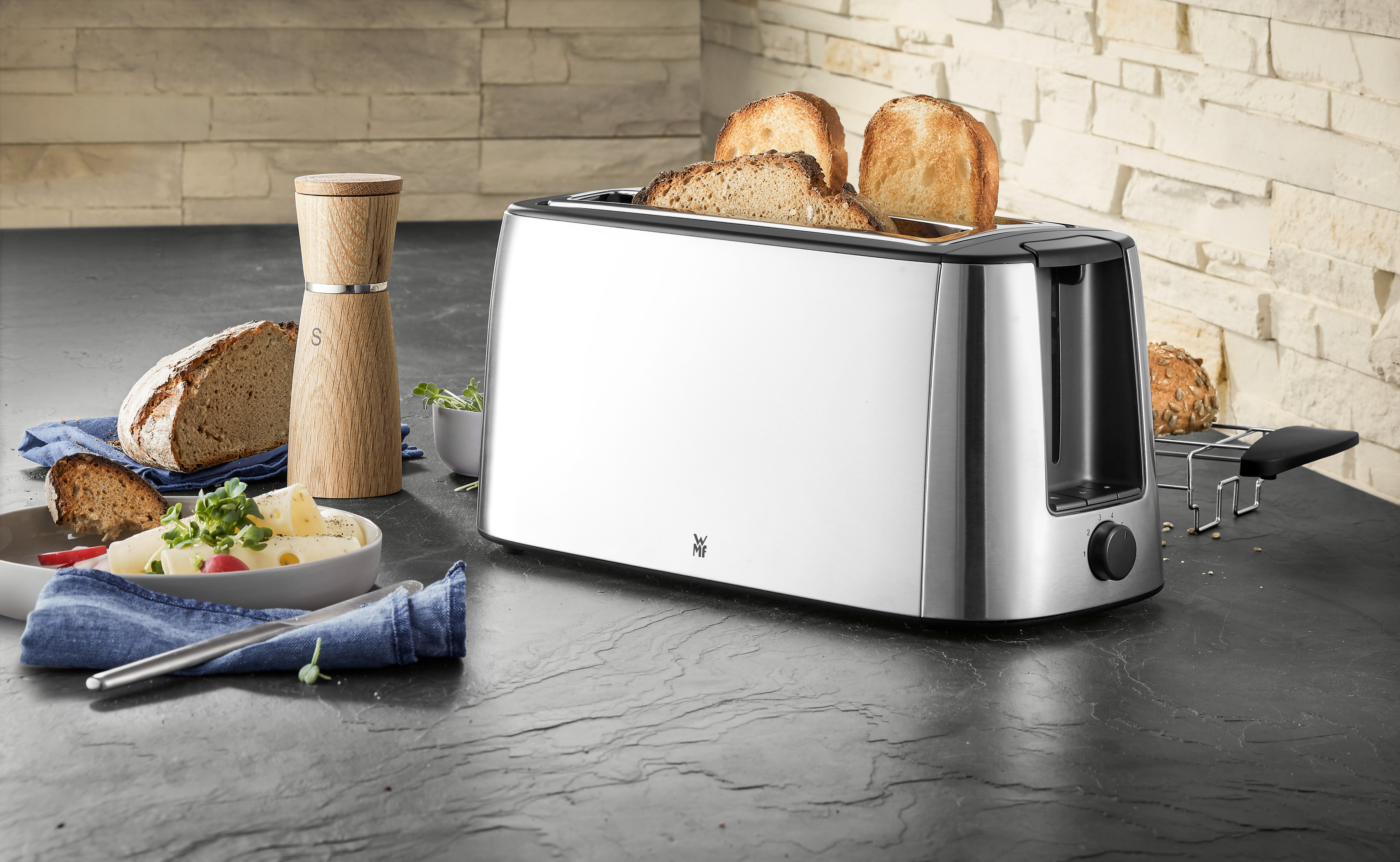 Toaster aus Edelstahl mit Toast, Brot und einem hölzernen Salzstreuer auf einer Arbeitsplatte.