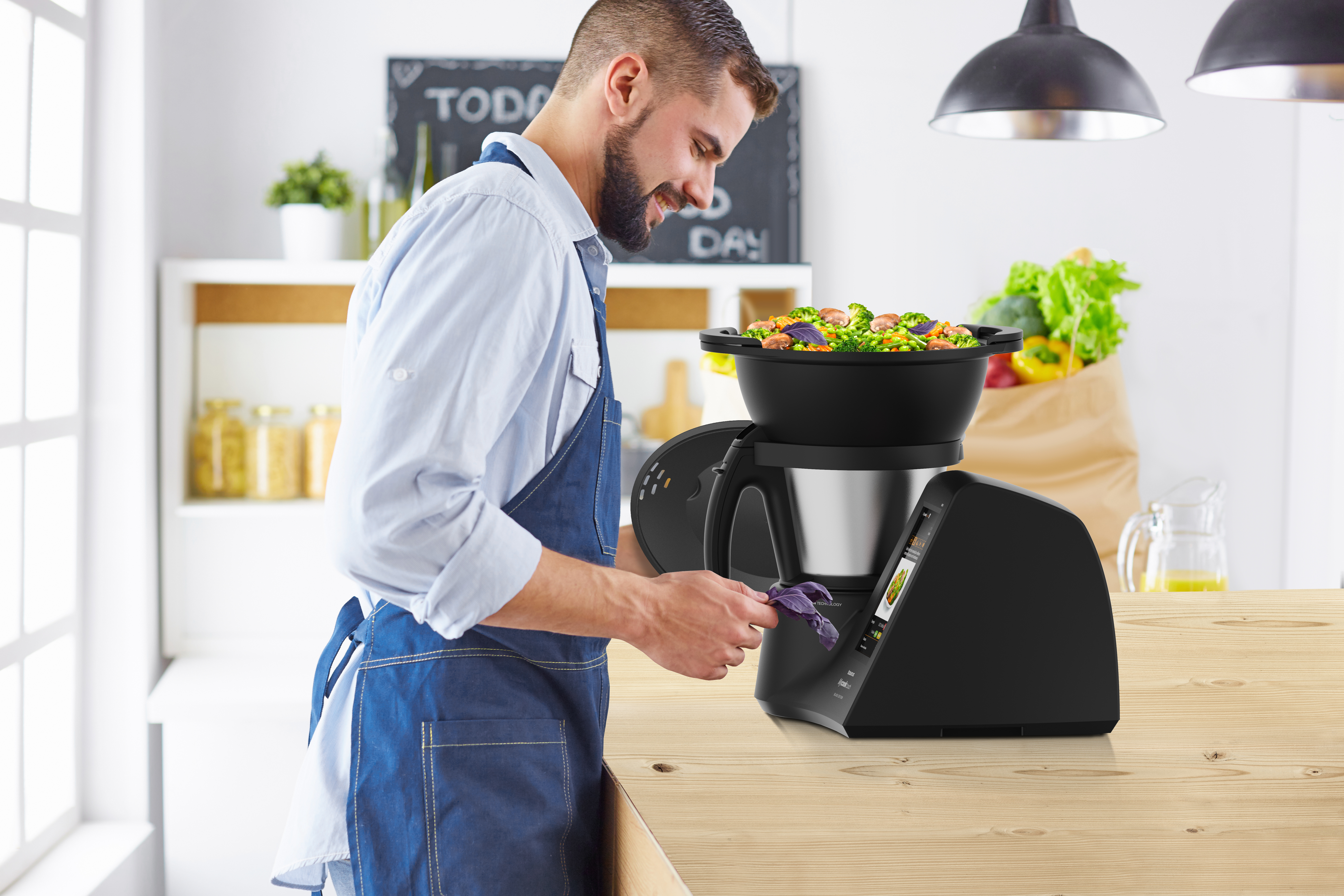 Un hombre con delantal prepara comida en un electrodoméstico de cocina negro sobre una encimera.