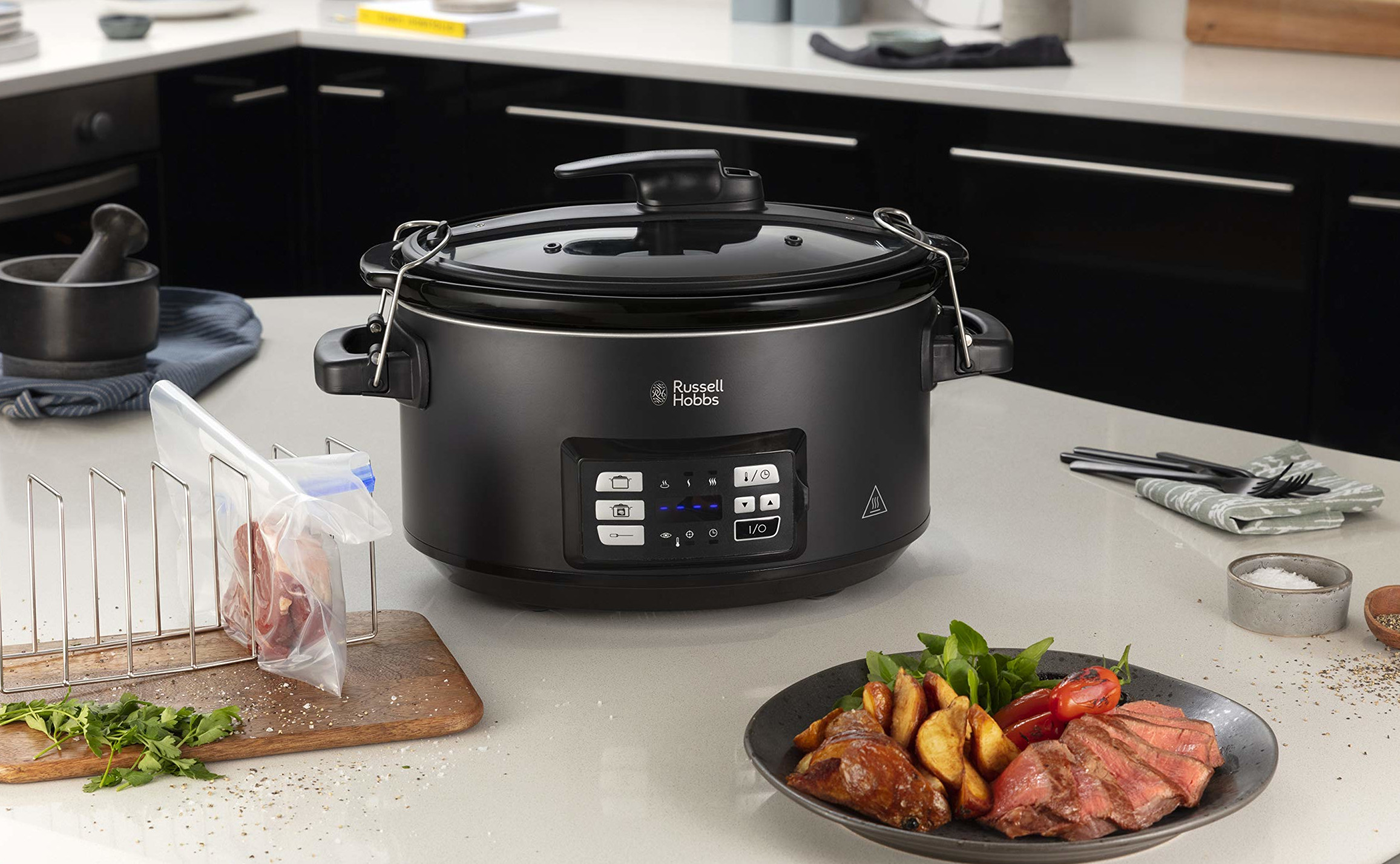 A black slow cooker on a counter with food, a cutting board, and other utensils.