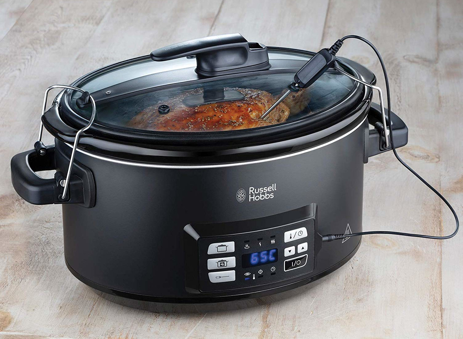 A black slow cooker with a glass lid. A thermometer is inserted into the food inside.