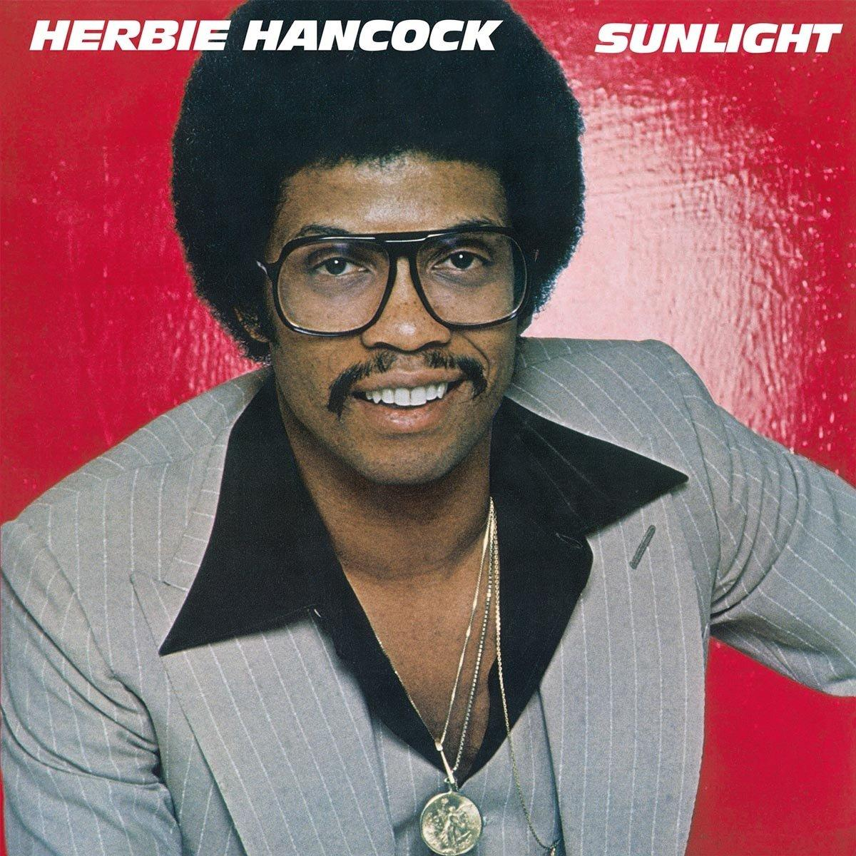 Herbie Hancock 'Sunlight' albumának borítója. Hancock szürke öltönyben, szemüvegben, mosolyogva, piros háttéren.