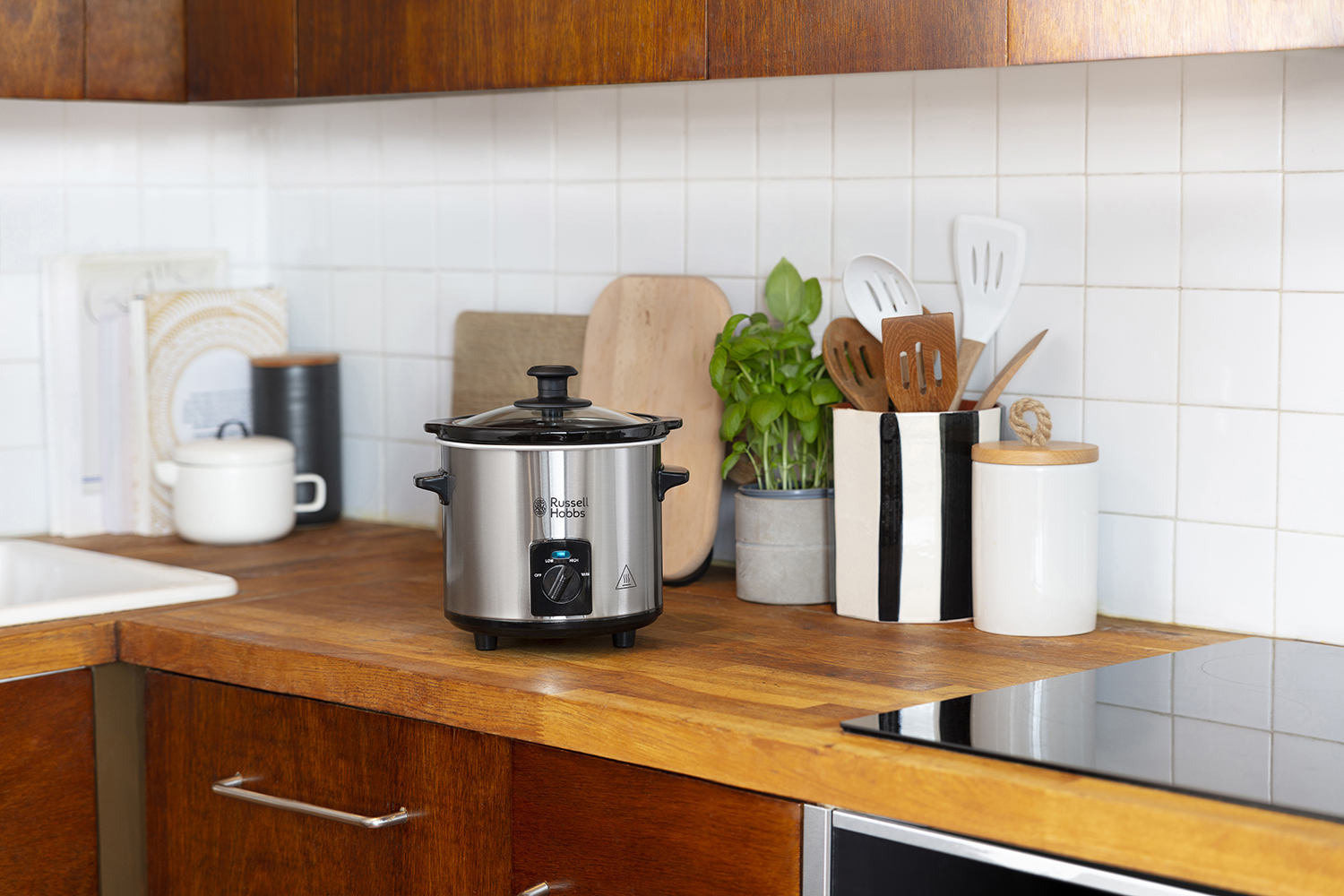 Kitchen scene with a silver slow cooker, wooden countertop, and various kitchen utensils.