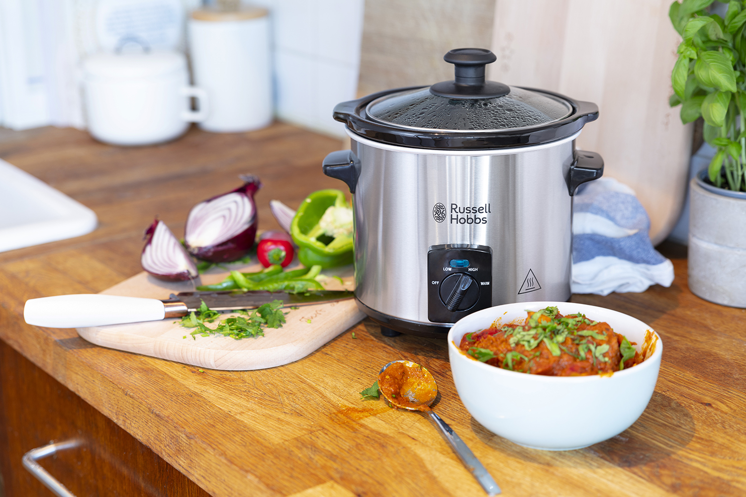 Kitchen scene with a slow cooker, vegetables, and a bowl of food.