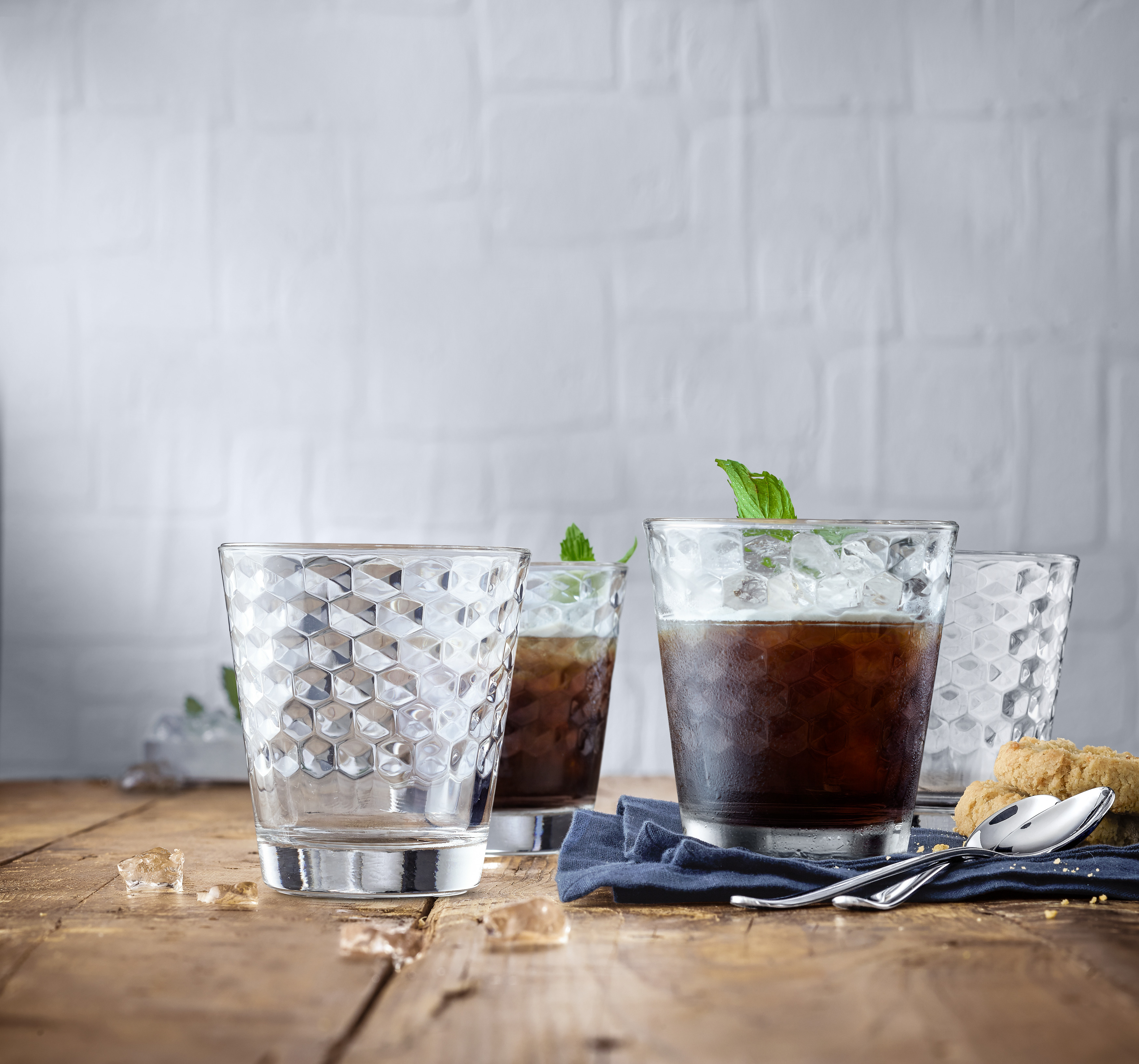Vier Gläser mit Eis, Kaffee und Minze auf einem Holztisch.