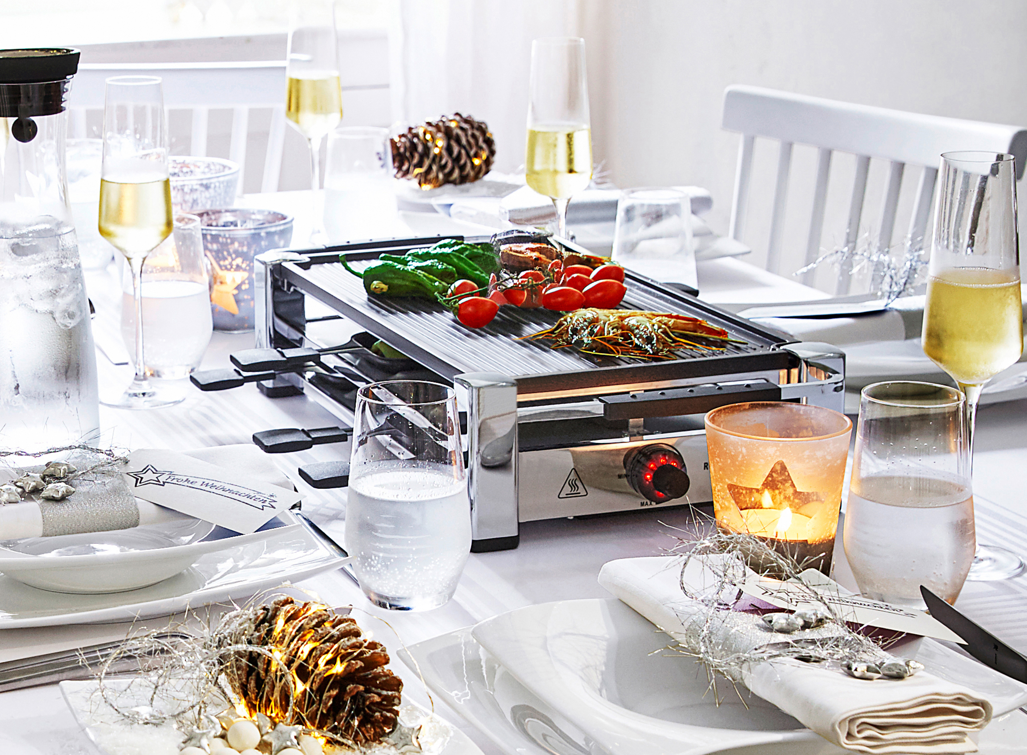 Tisch mit Essen, Raclette-Grill, Champagner und Kerzen. Festlich.
