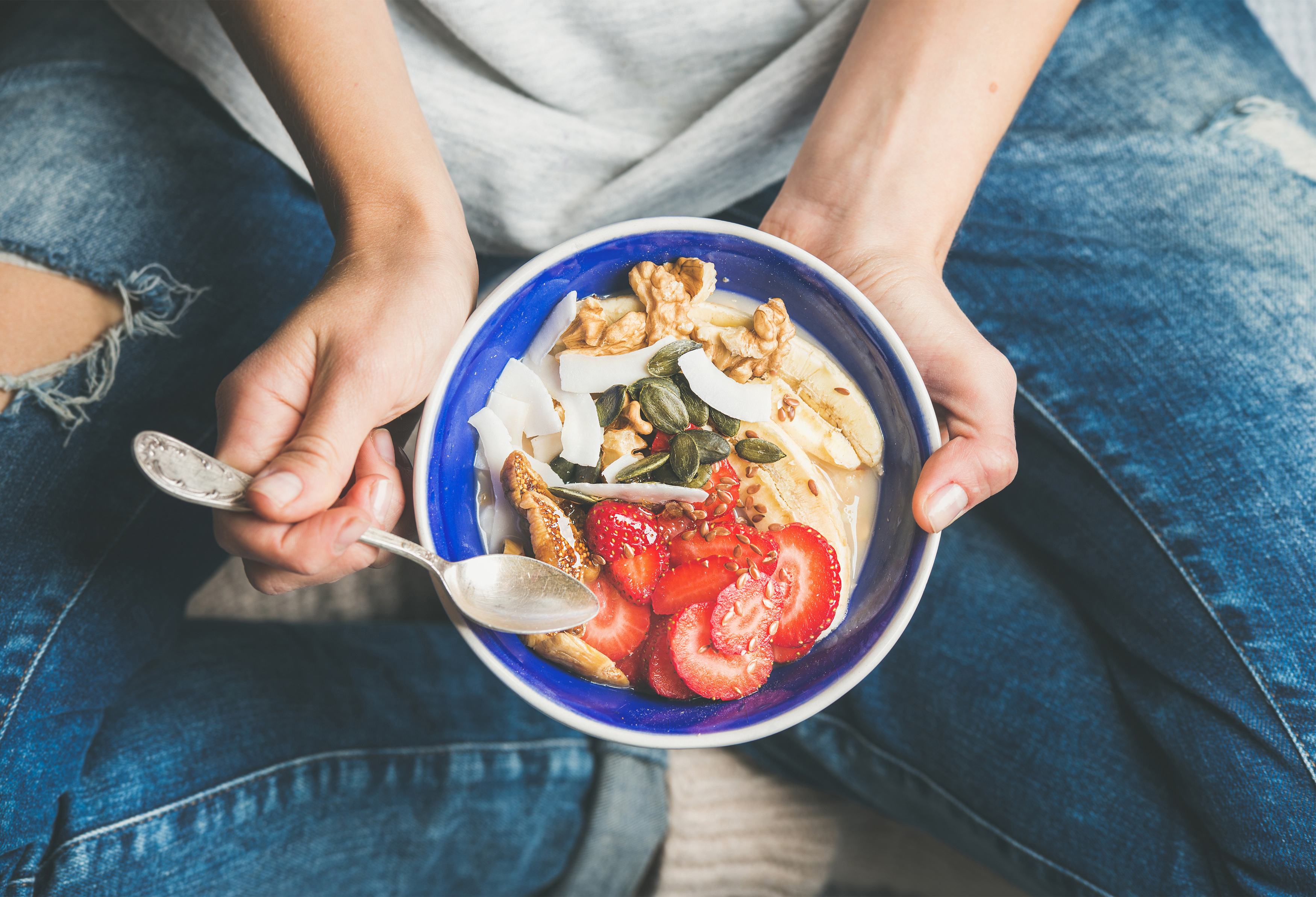 Person hält eine Schüssel mit Essen mit Erdbeeren, Nüssen und Samen. Jeans.