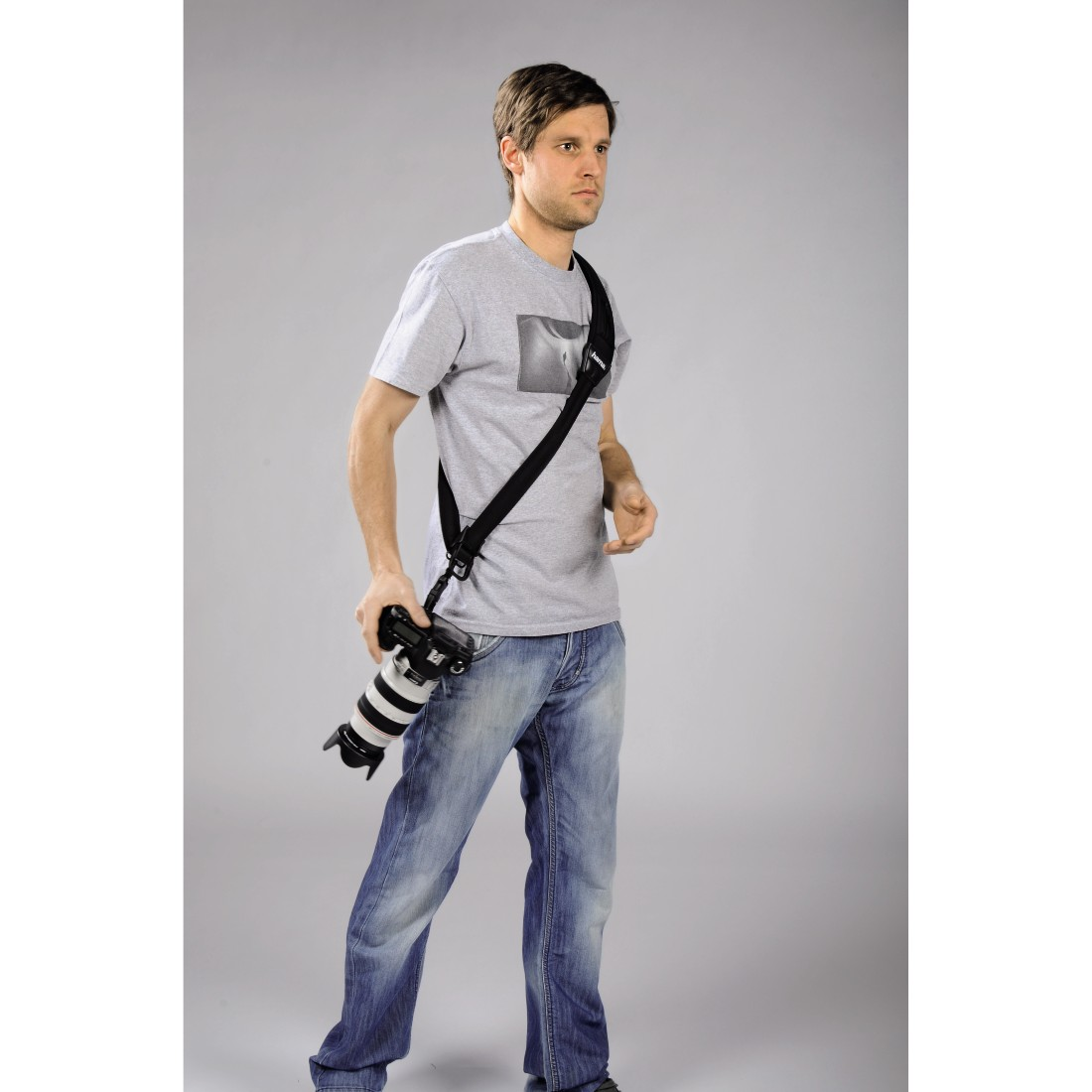 Een man met een camera over zijn schouder, draagt jeans en een grijs t-shirt.