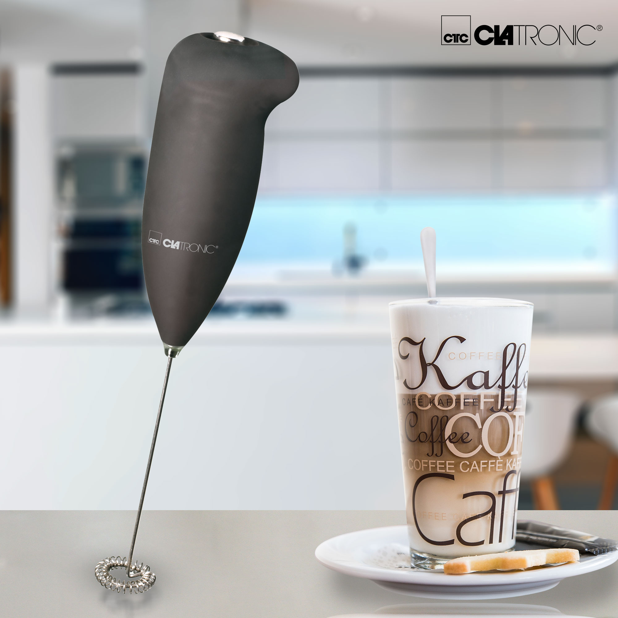 Ein schwarzer Milchaufschäumer mit einem Glas Kaffee mit einer Kaffeezeichnung auf einem weißen Teller.