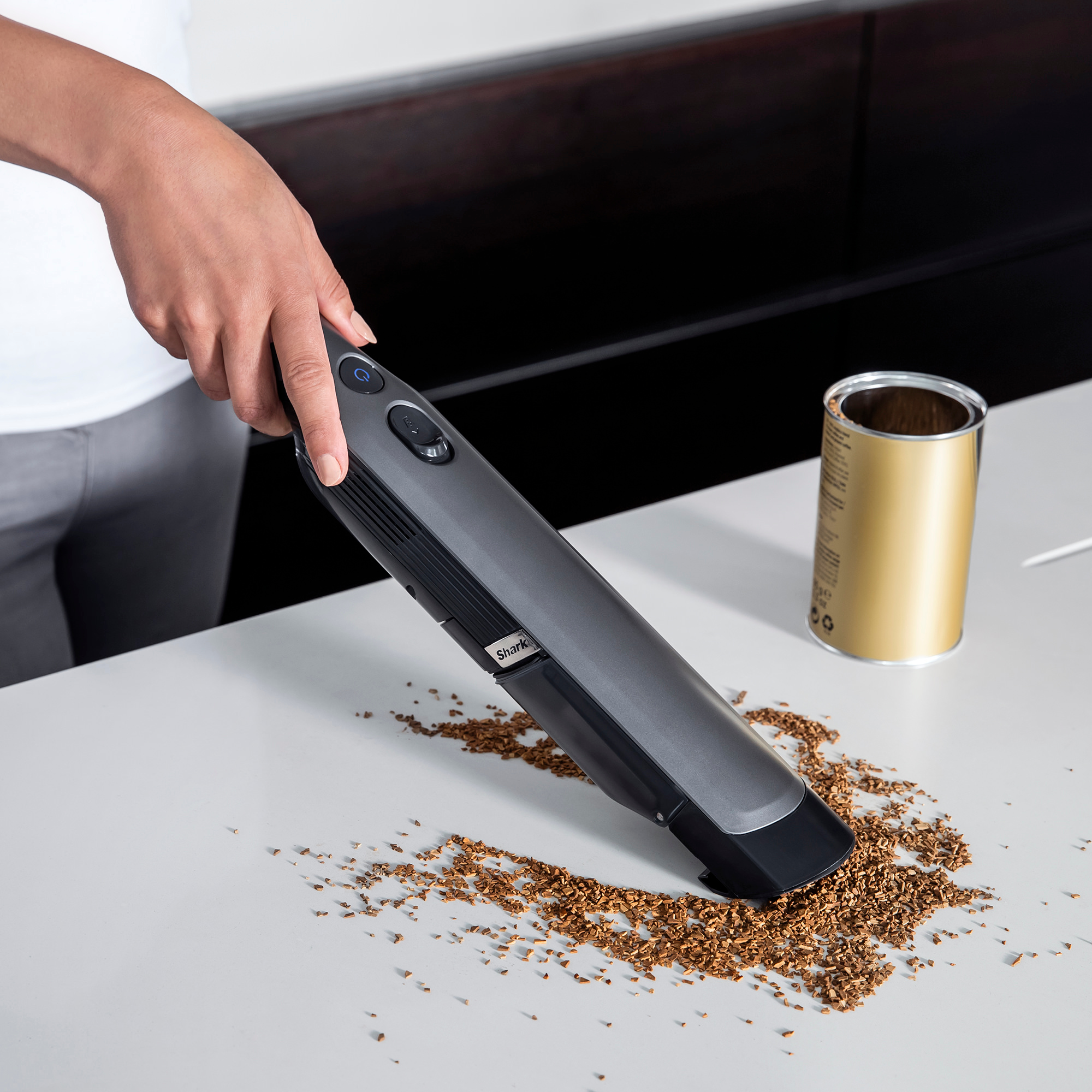Person saugt braune Ablagerungen auf einer weißen Oberfläche mit einem Handstaubsauger.