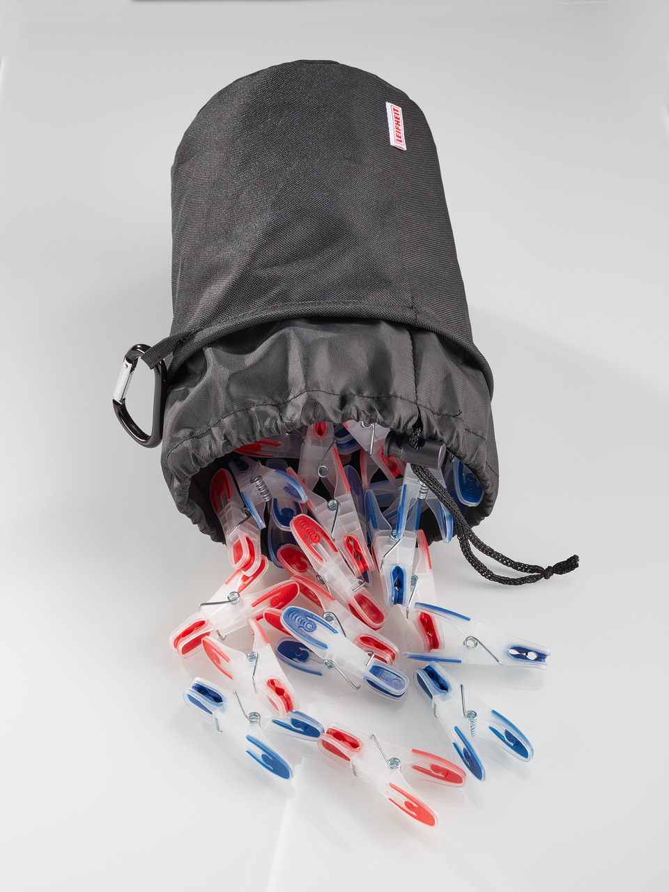 Eine graue Tasche, aus der Wäscheklammern herausfallen. Die Klammern sind rot, weiß und blau.