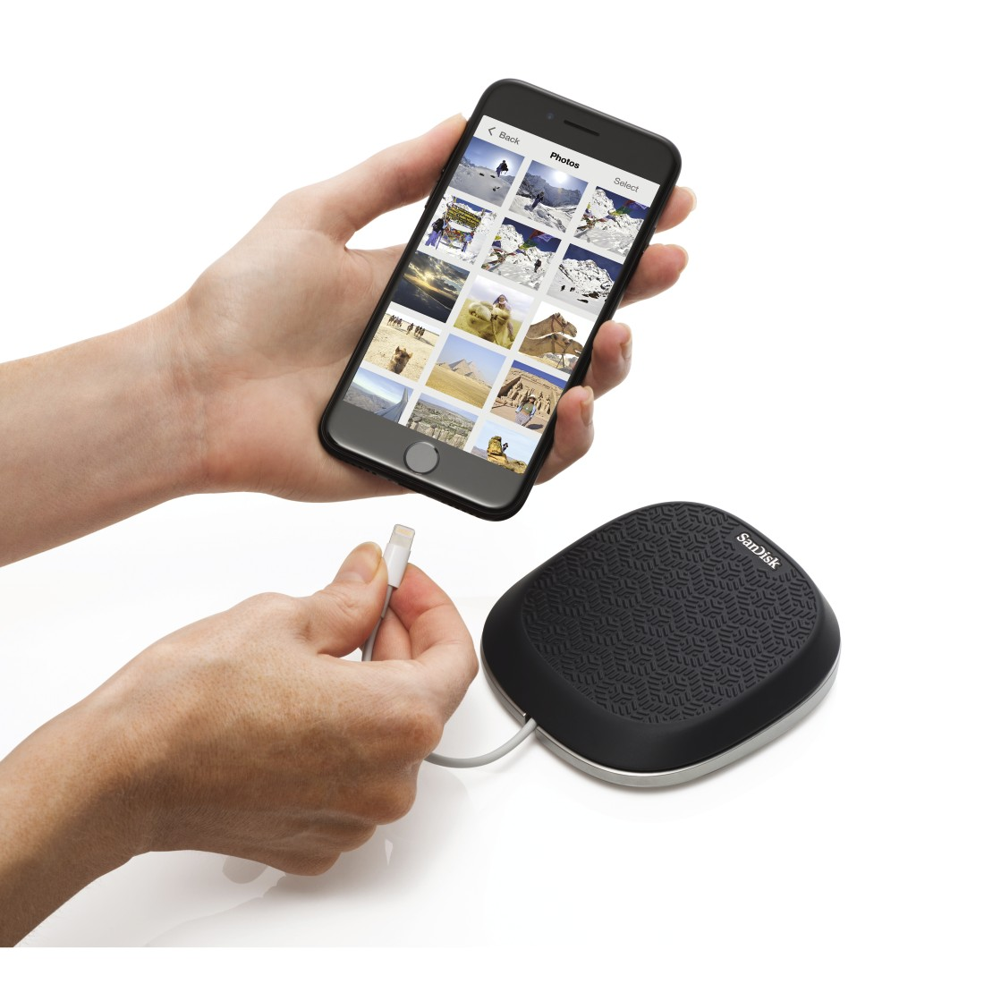 Hands holding a phone displaying photos, connected to a black, rounded device with cable.