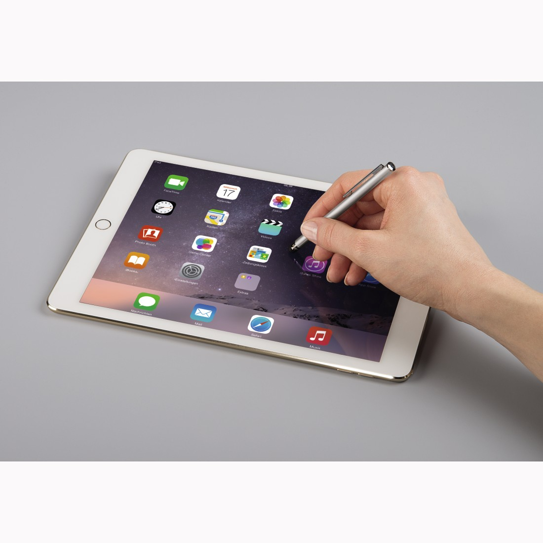 A hand holding a silver stylus on a white iPad with app icons on the screen.