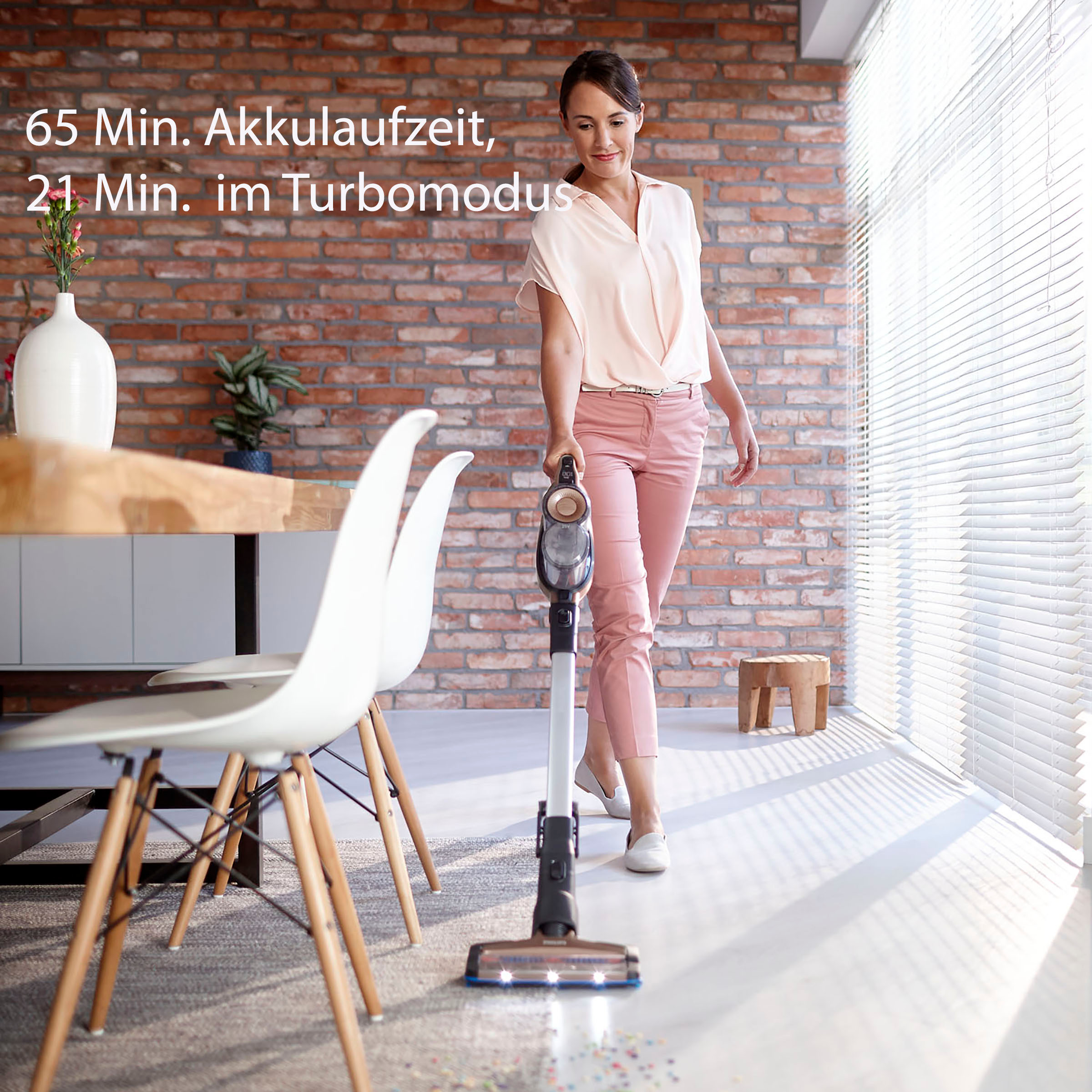 Eine Frau, die einen kabellosen Staubsauger in einem Raum mit Backsteinmauer und Fenster benutzt.