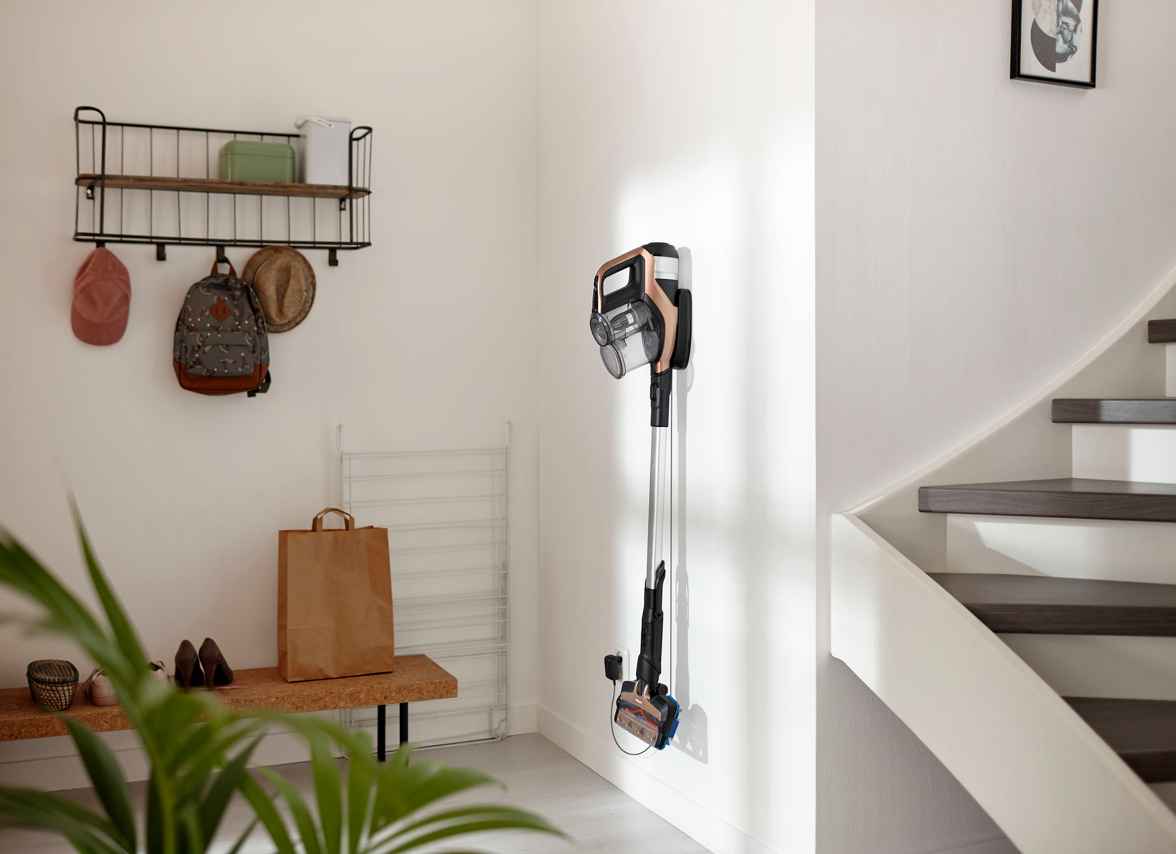 Ein kabelloser Staubsauger an einer weißen Wand neben einer Treppe montiert.