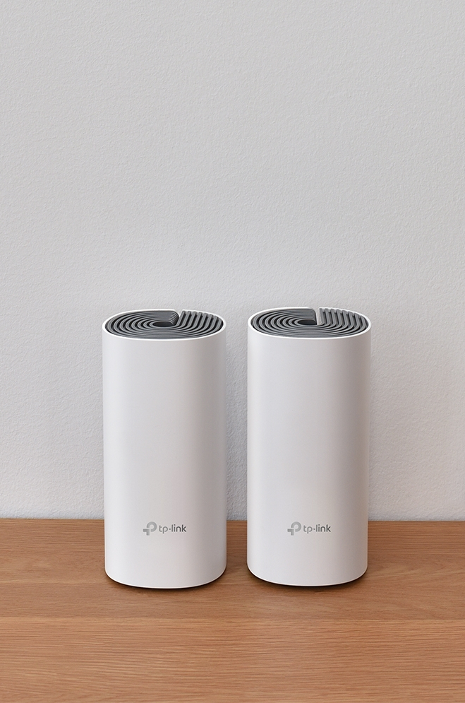 Deux appareils wifi mesh TP-Link blancs sur une table en bois contre un mur blanc.