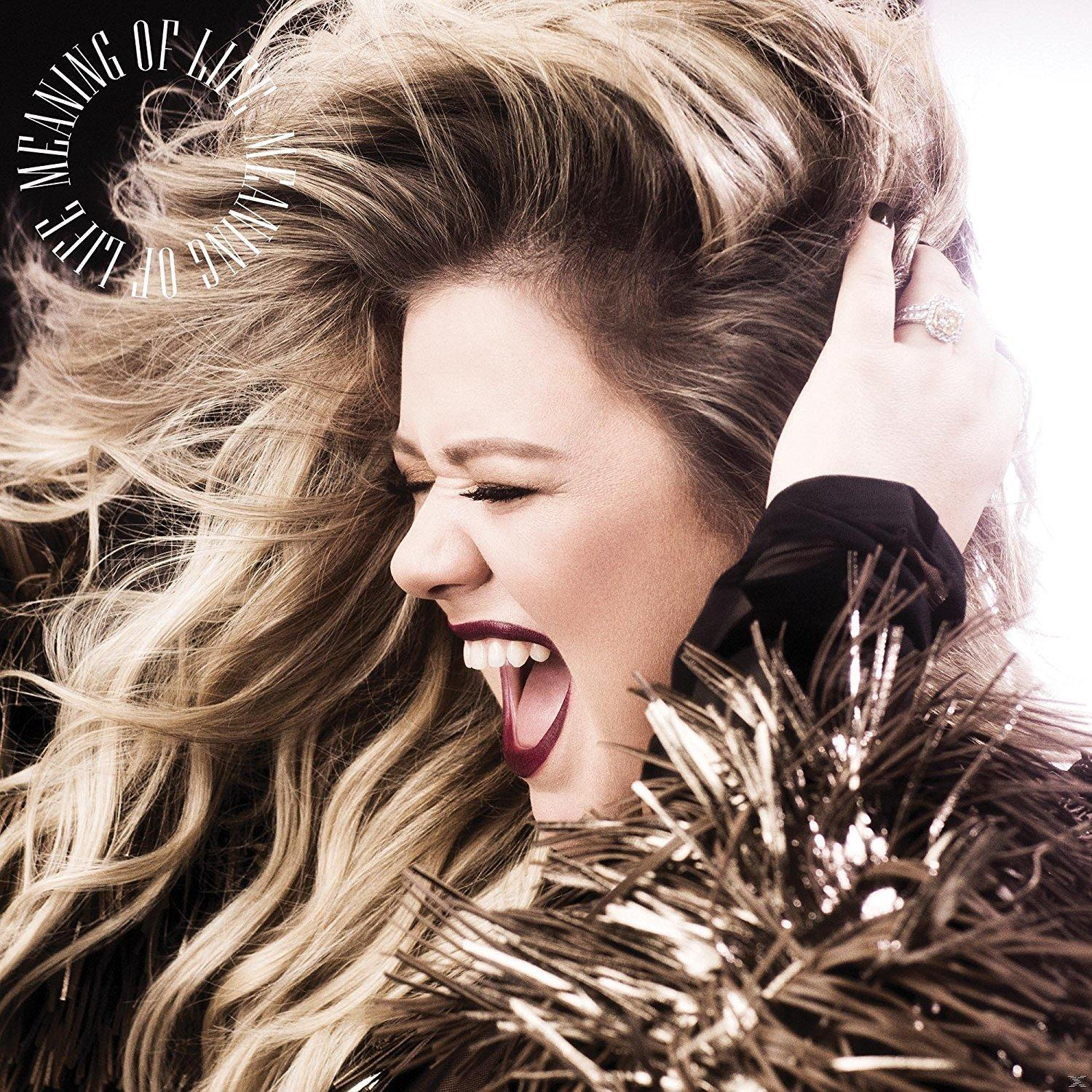 Vrouw met lang blond haar, mond open. Ze draagt een zwarte top met een verenboa. De albumtitel is "Meaning of Life".