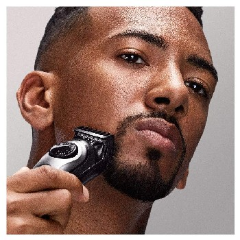 Hombre afeitándose la barba con una recortadora negra y plateada.