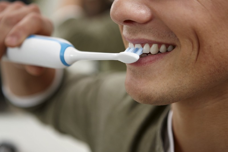 Un hombre cepillándose los dientes con un cepillo eléctrico. Primer plano, enfoque en la boca.