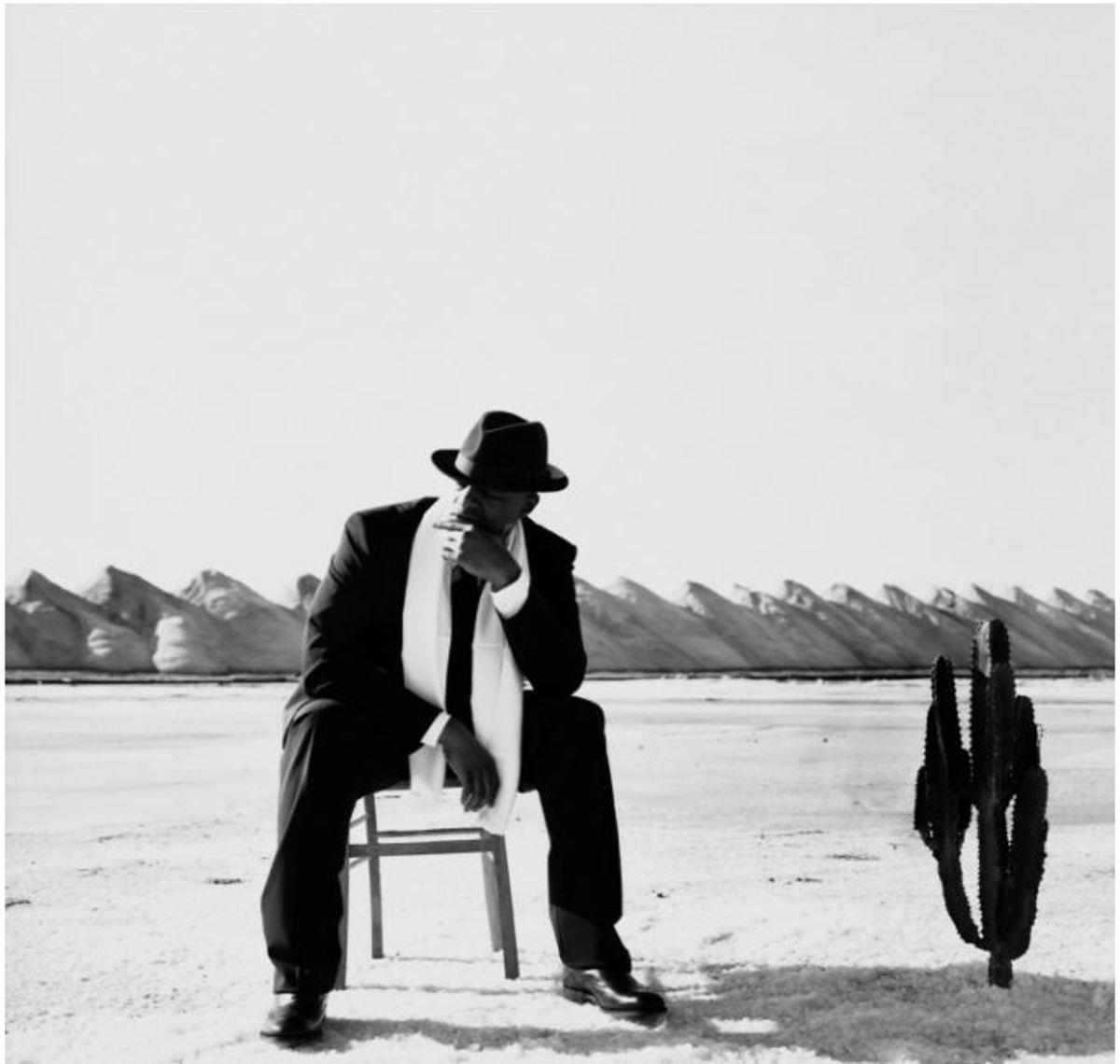 Une photo en noir et blanc d'un homme en costume, assis sur une chaise dans un paysage désertique.