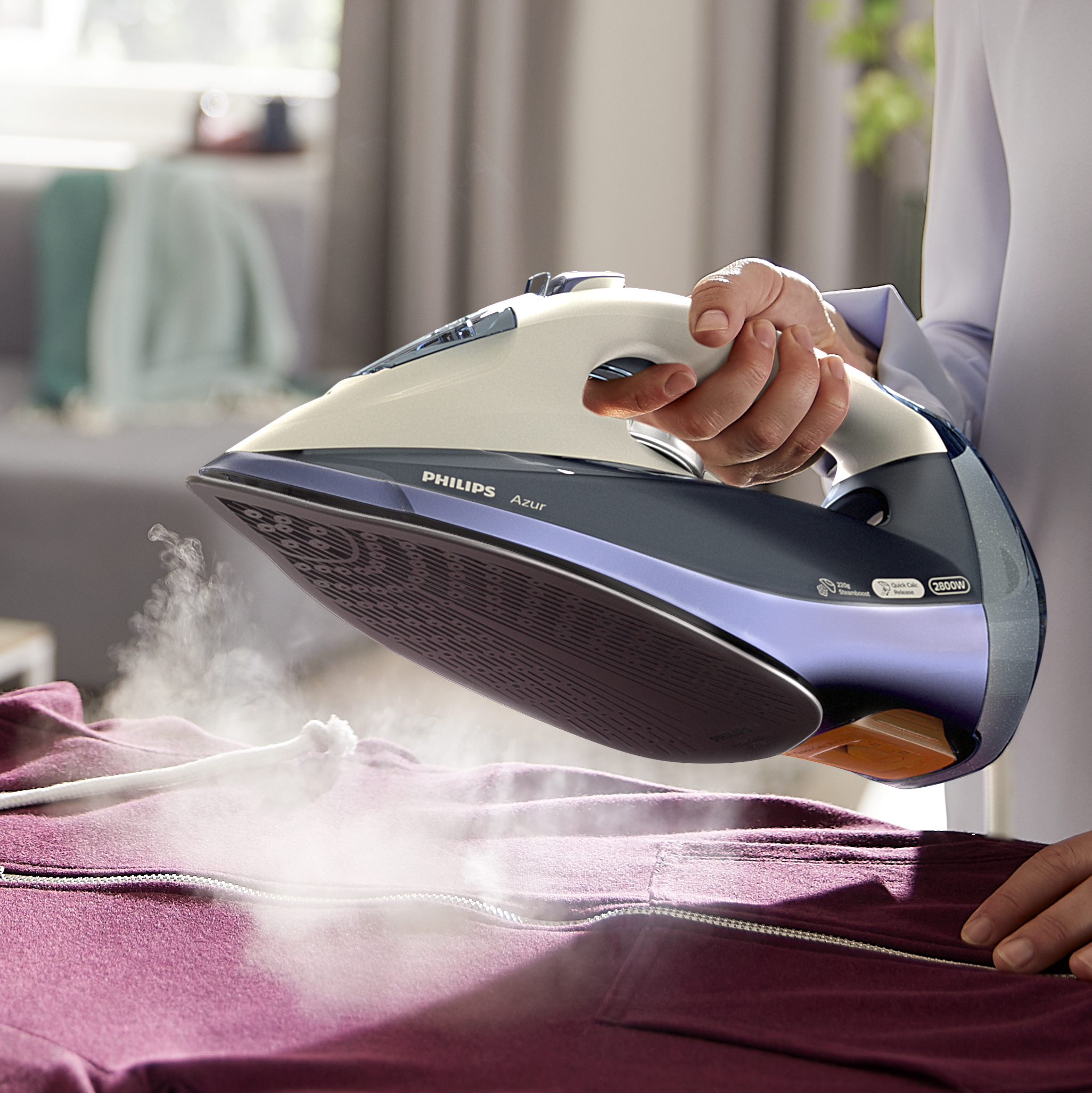 Bir kişi, Philips Azur ütüsü ile bordo bir kapüşonluyu ütülüyor, buhar görünüyor.