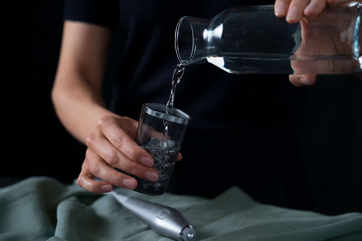 A person pouring water from a clear glass jug into a glass.